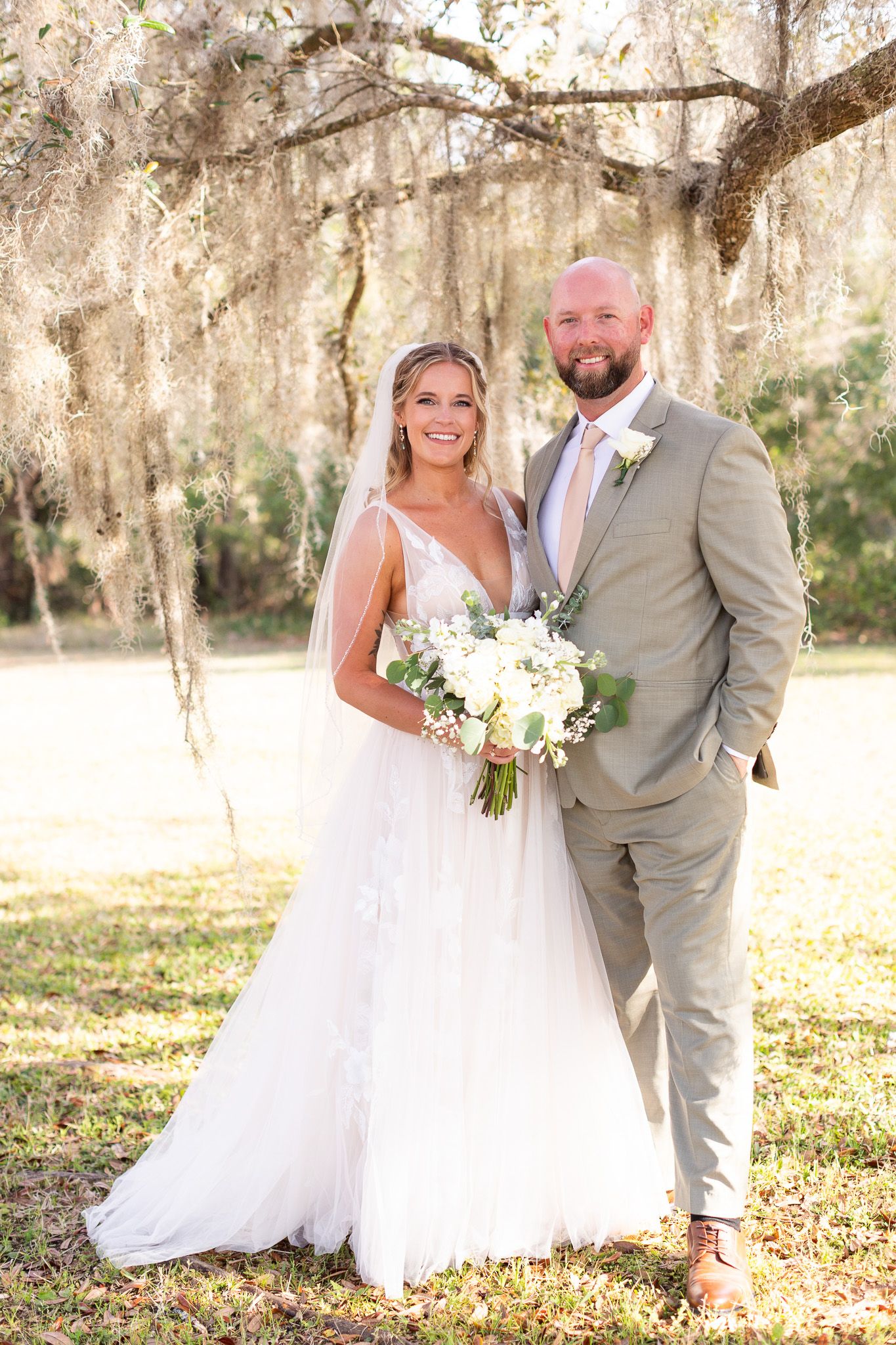 Wedding couple poses together under Spanish moss draped trees in outdoor setting.