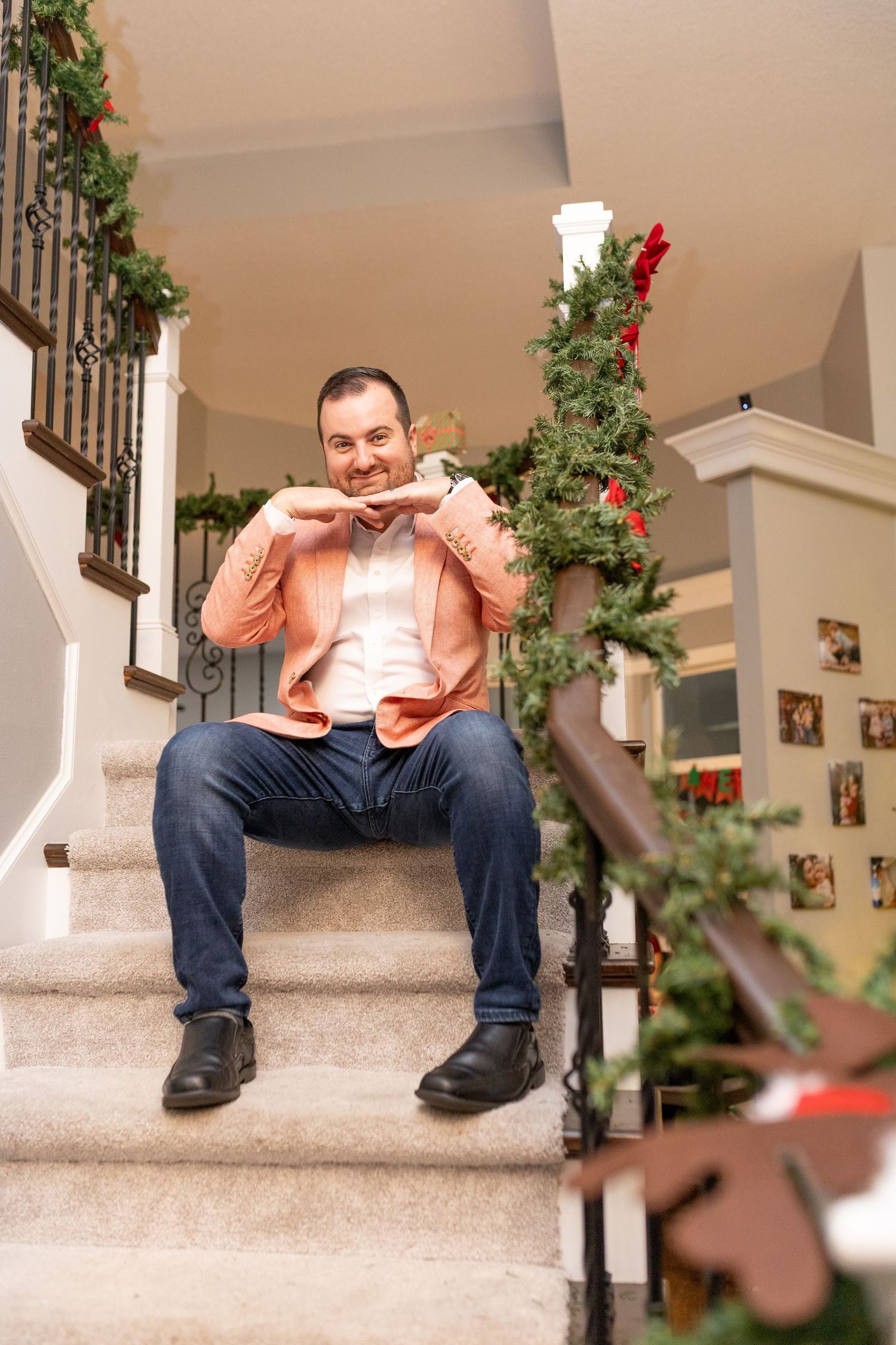 Someone wearing a peach-colored blazer and jeans sits on carpeted stairs decorated with holiday greenery.
