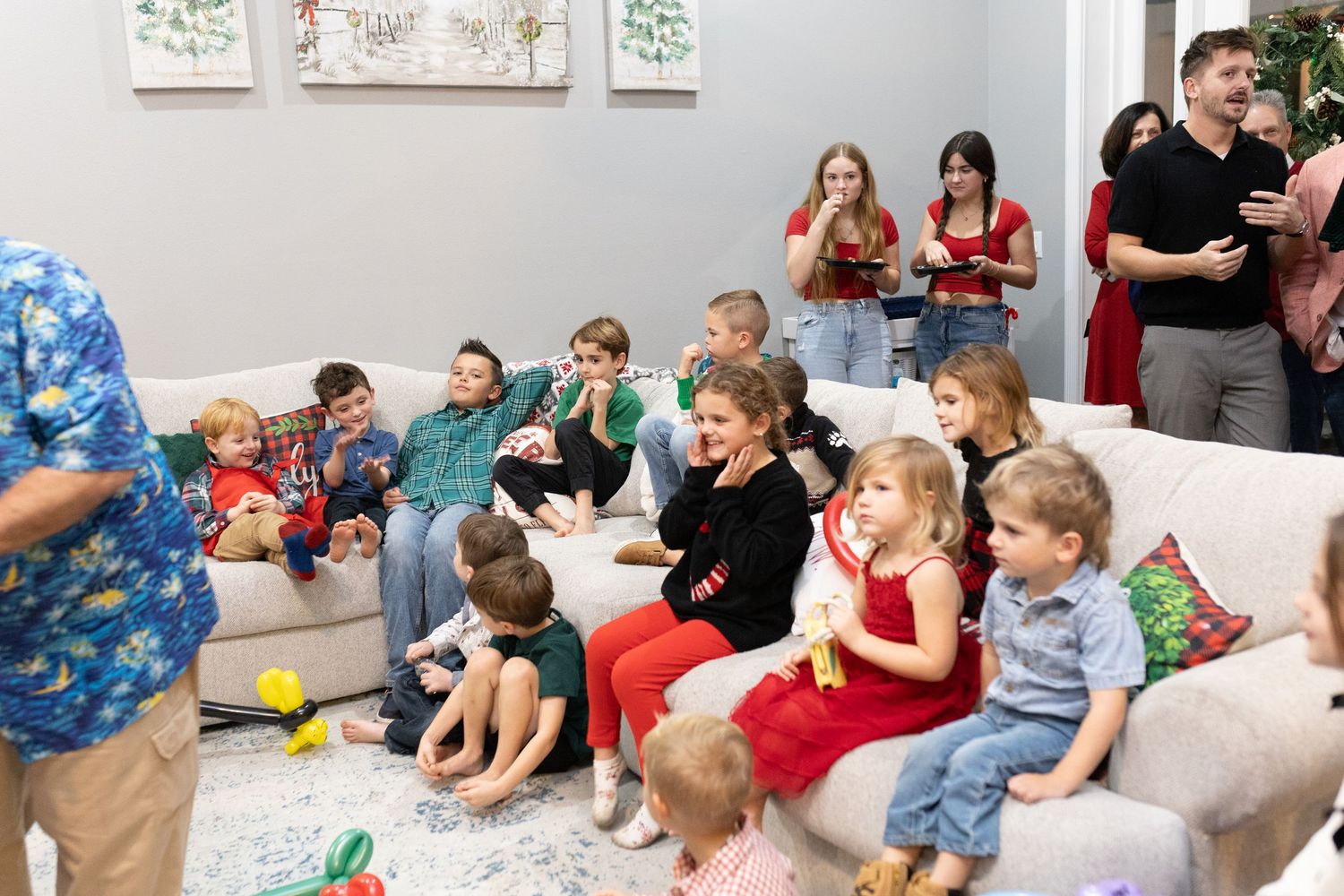 Children sit attentively on couches during a holiday event with wall decorations visible.