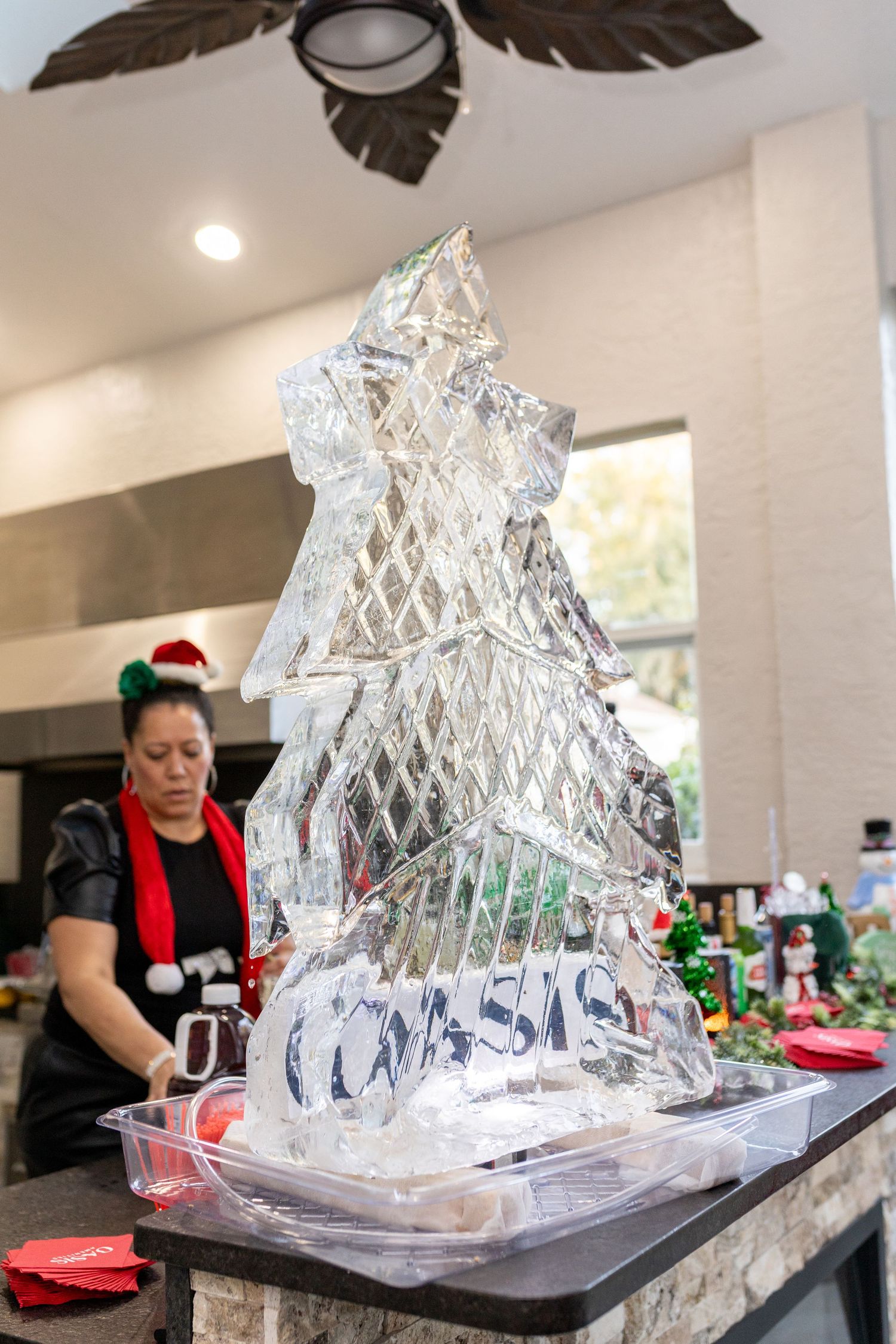 Intricate ice sculpture of a Christmas tree displayed on a counter at a holiday event.