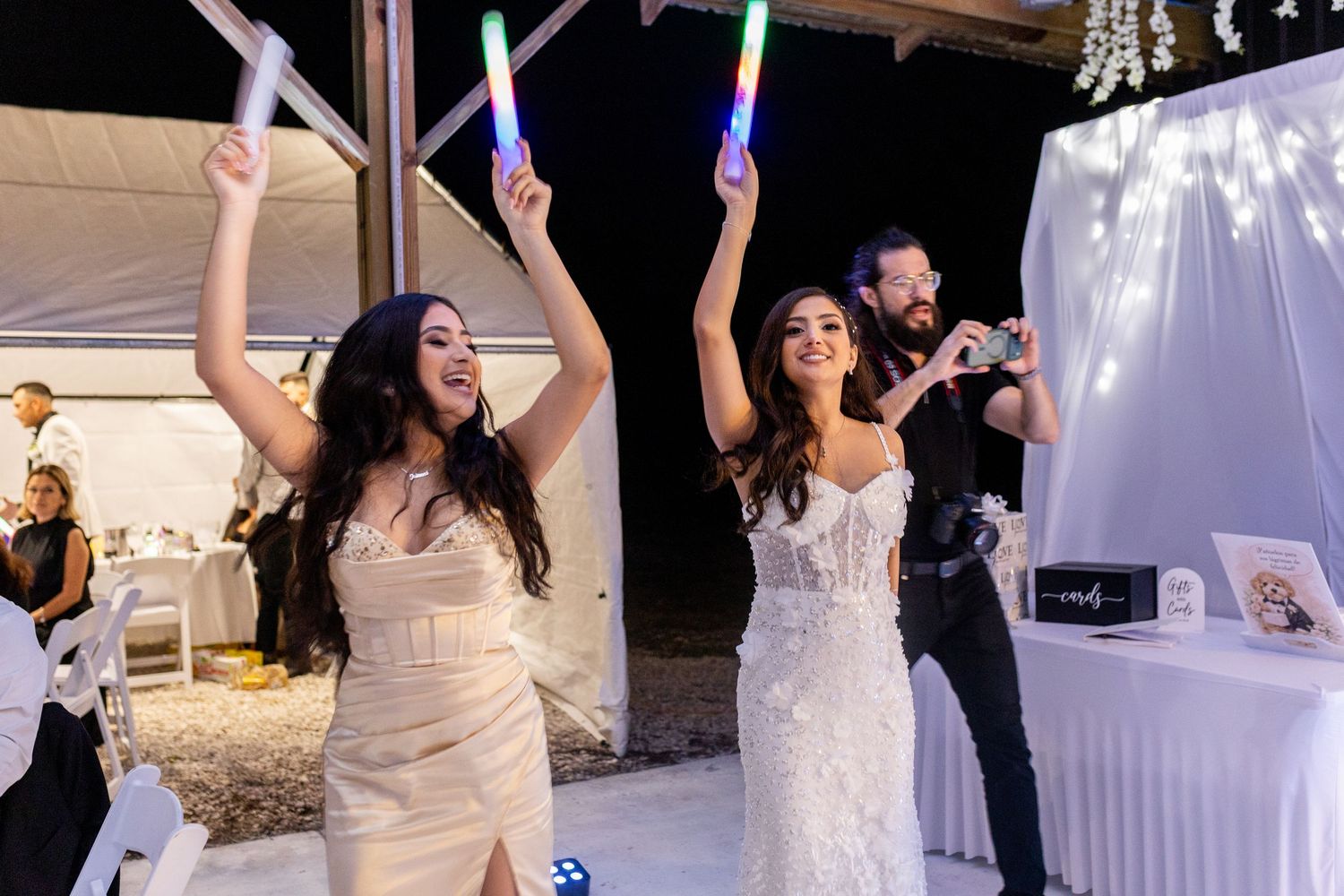 Wedding celebration with guests dancing and waving LED glow sticks in a decorated reception hall.