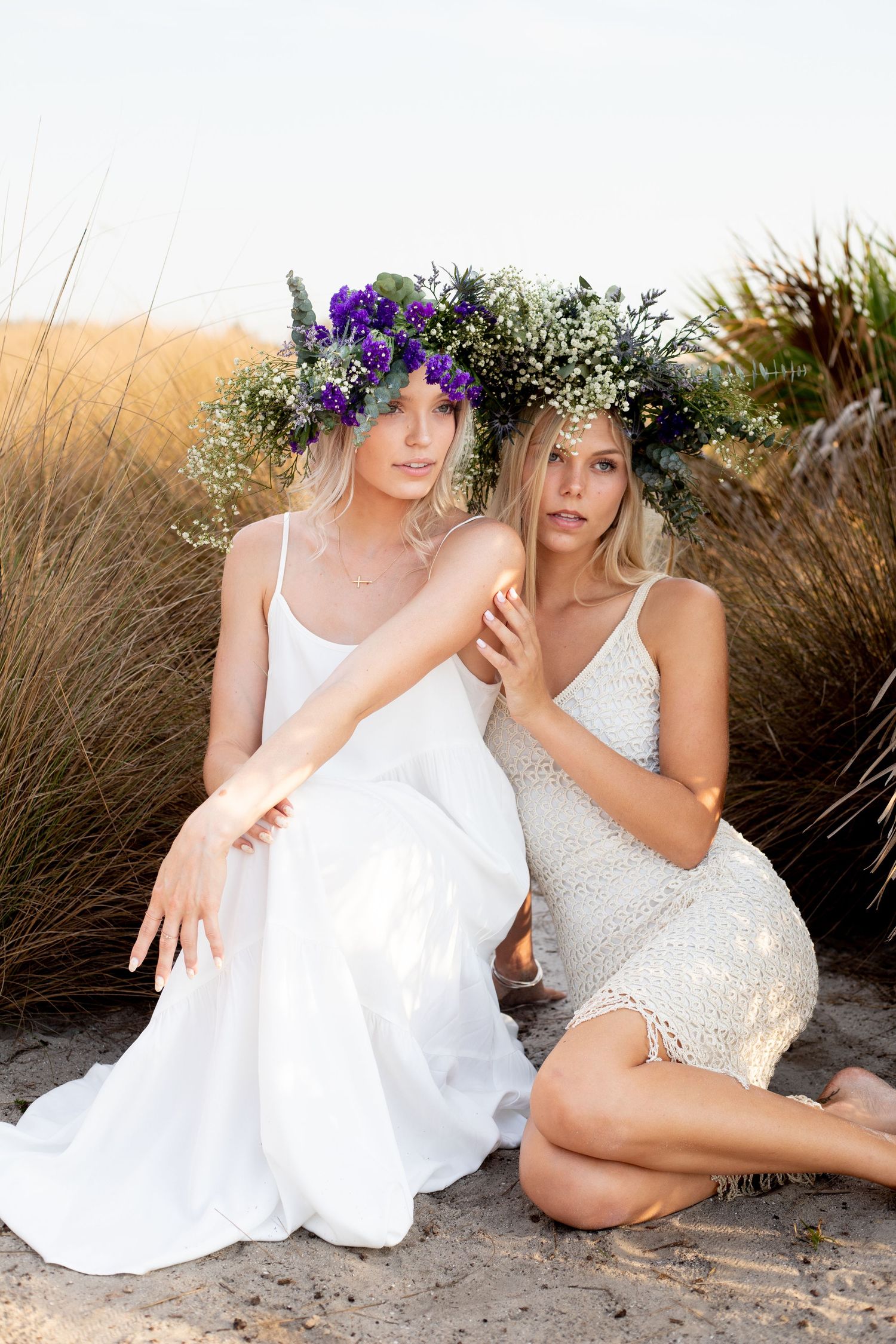 Beach photography session with white dresses and floral crowns at sunset.