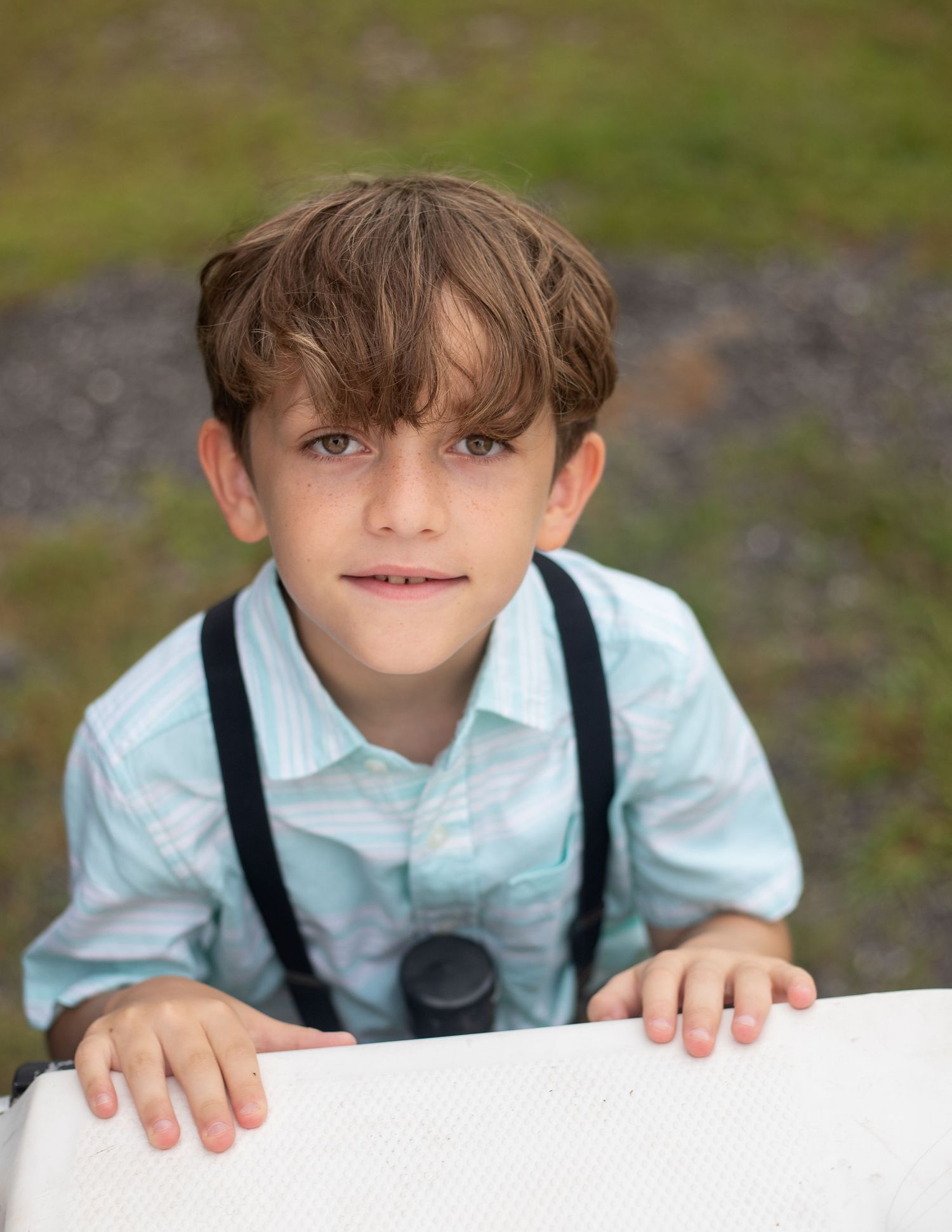 Child in vintage outfit peeks over white surface with playful expression.