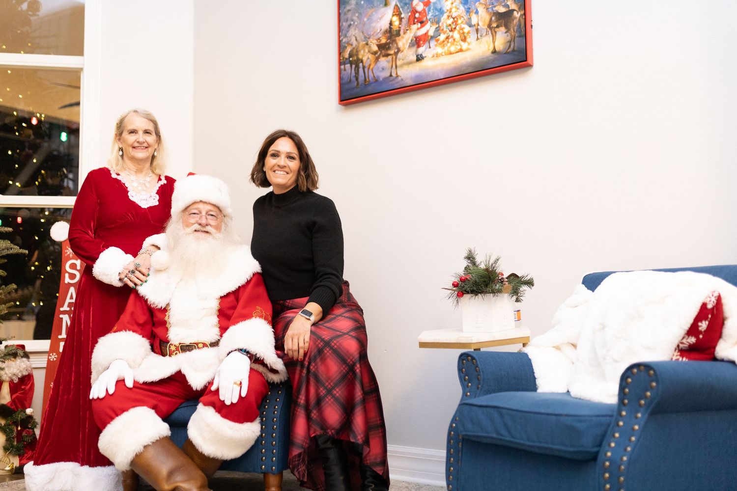 Holiday portraits with Santa Claus seated on blue chaise lounge against white wall.