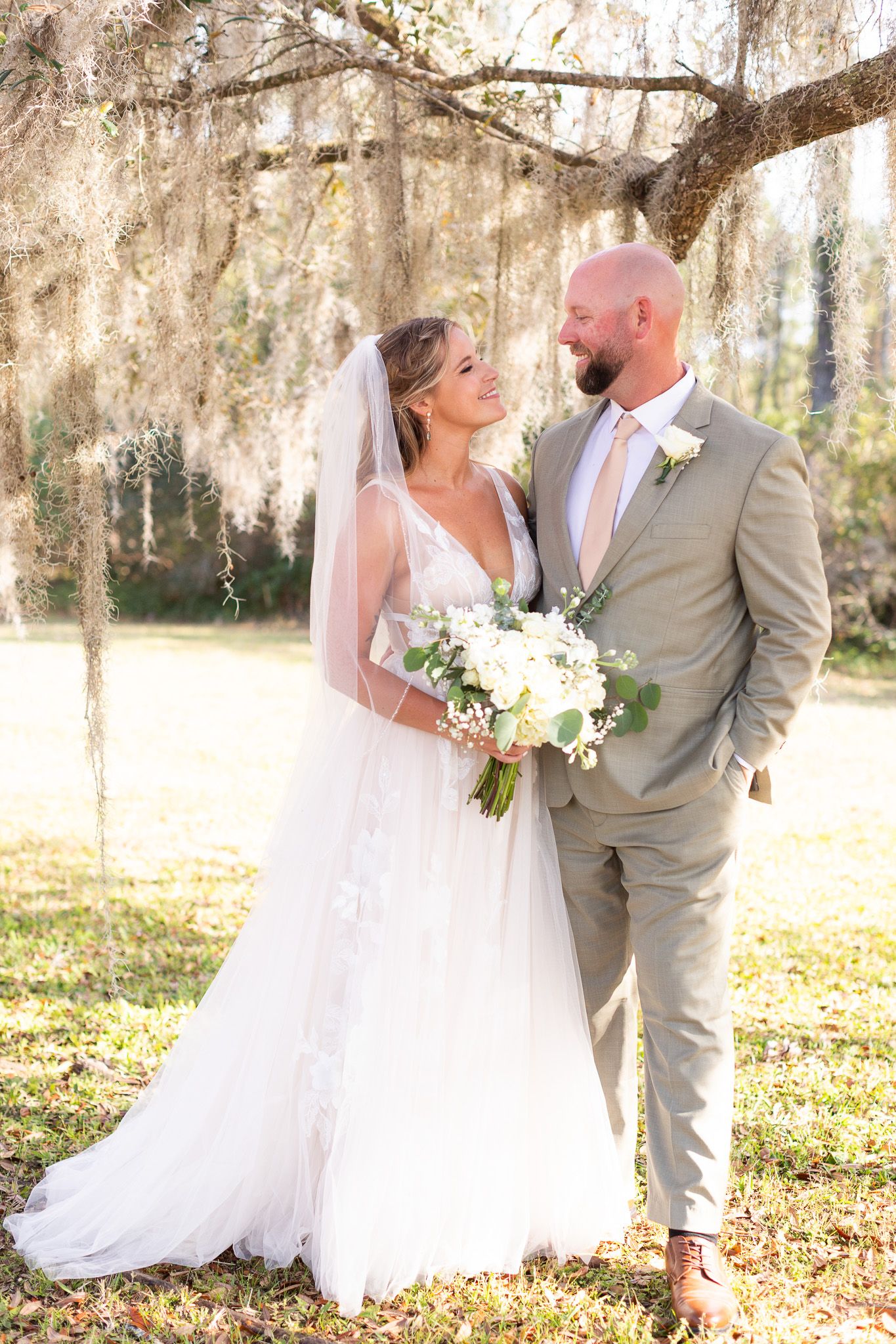 Newlyweds share romantic moment under moss-covered trees in natural light.