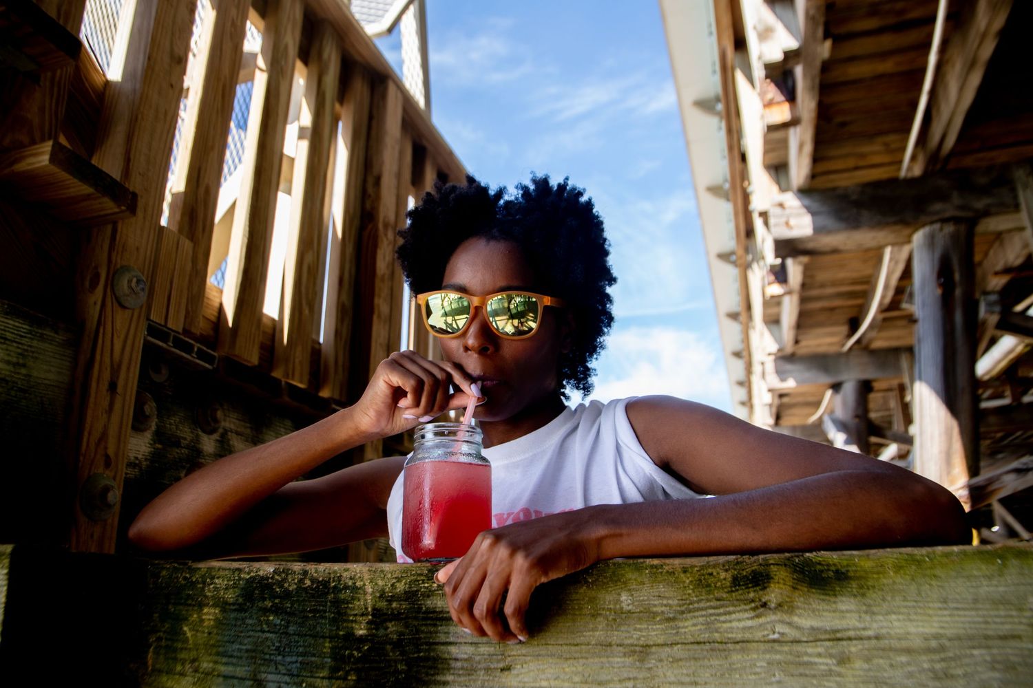 Beach lifestyle photo taken from below wooden pier with bright blue sky visible.