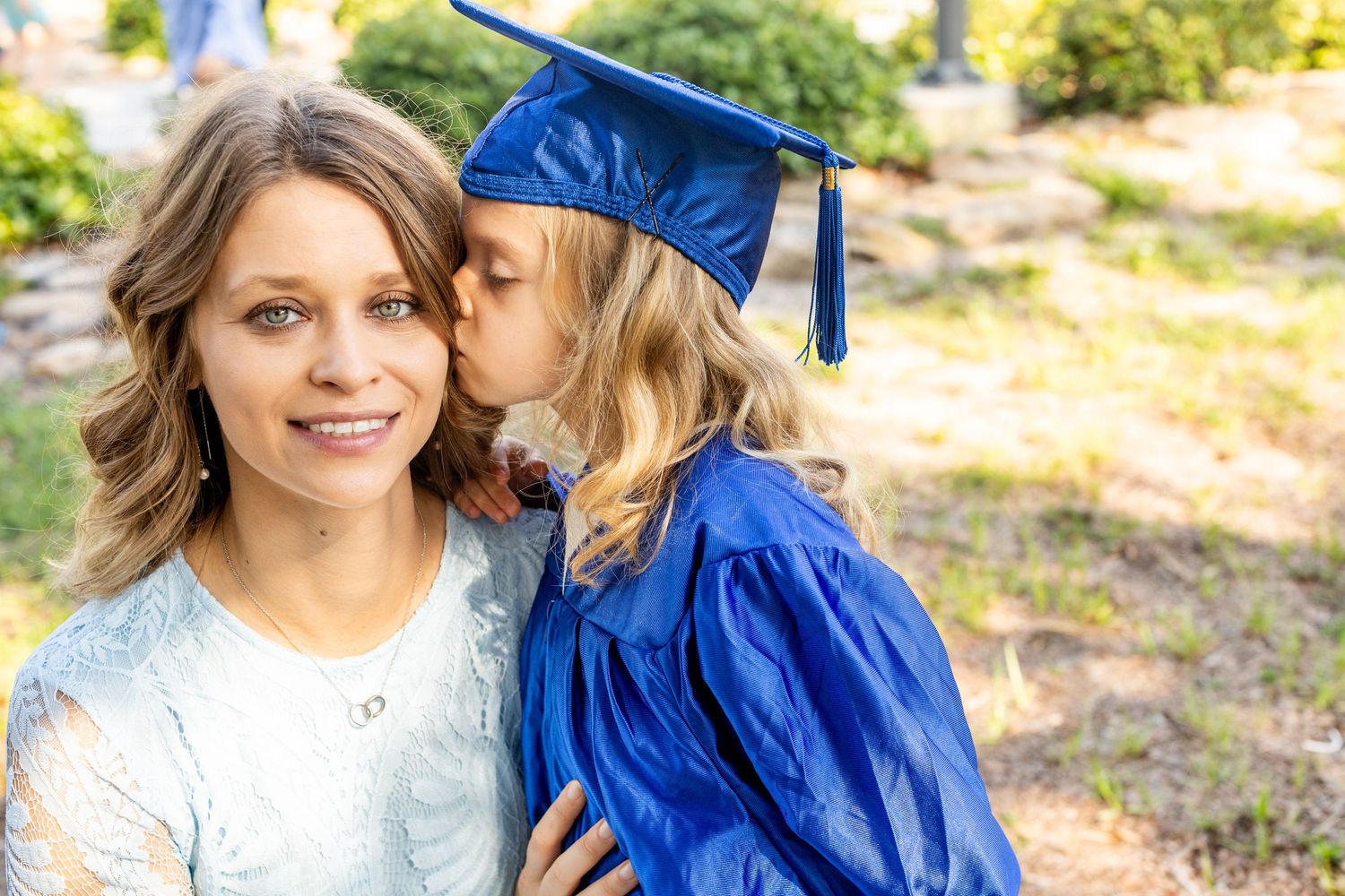 Mother and child sharing tender moment during graduation celebration in outdoor setting.