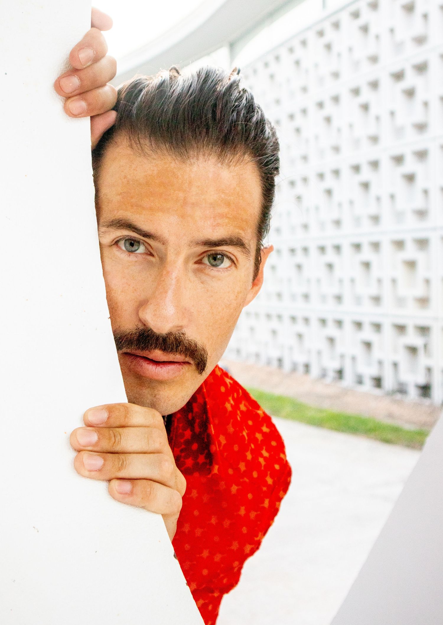 Artistic portrait through white geometric frame featuring a red shirt and mustache.