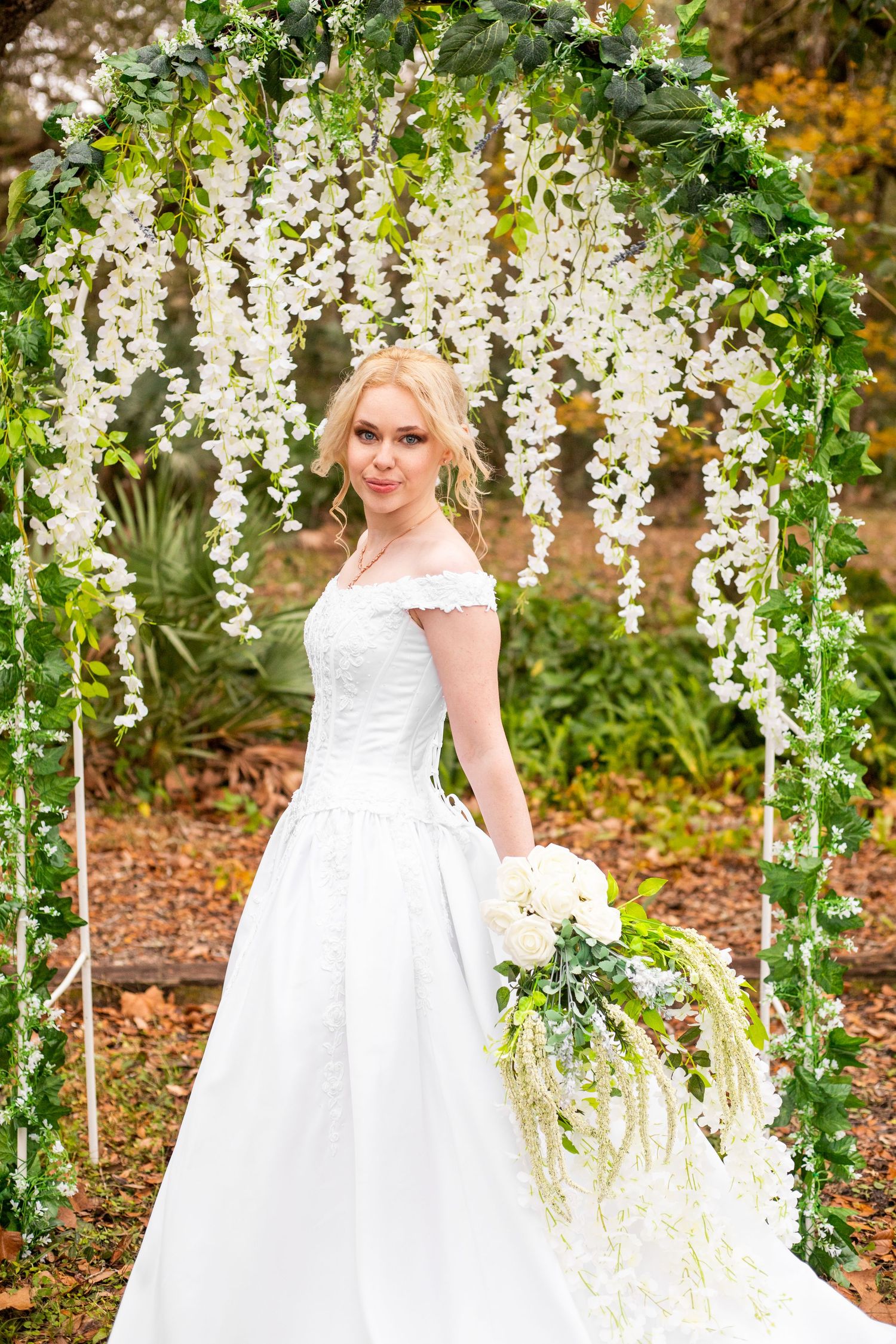 A beautiful outdoor bridal portrait features cascading white floral decorations and autumn scenery.