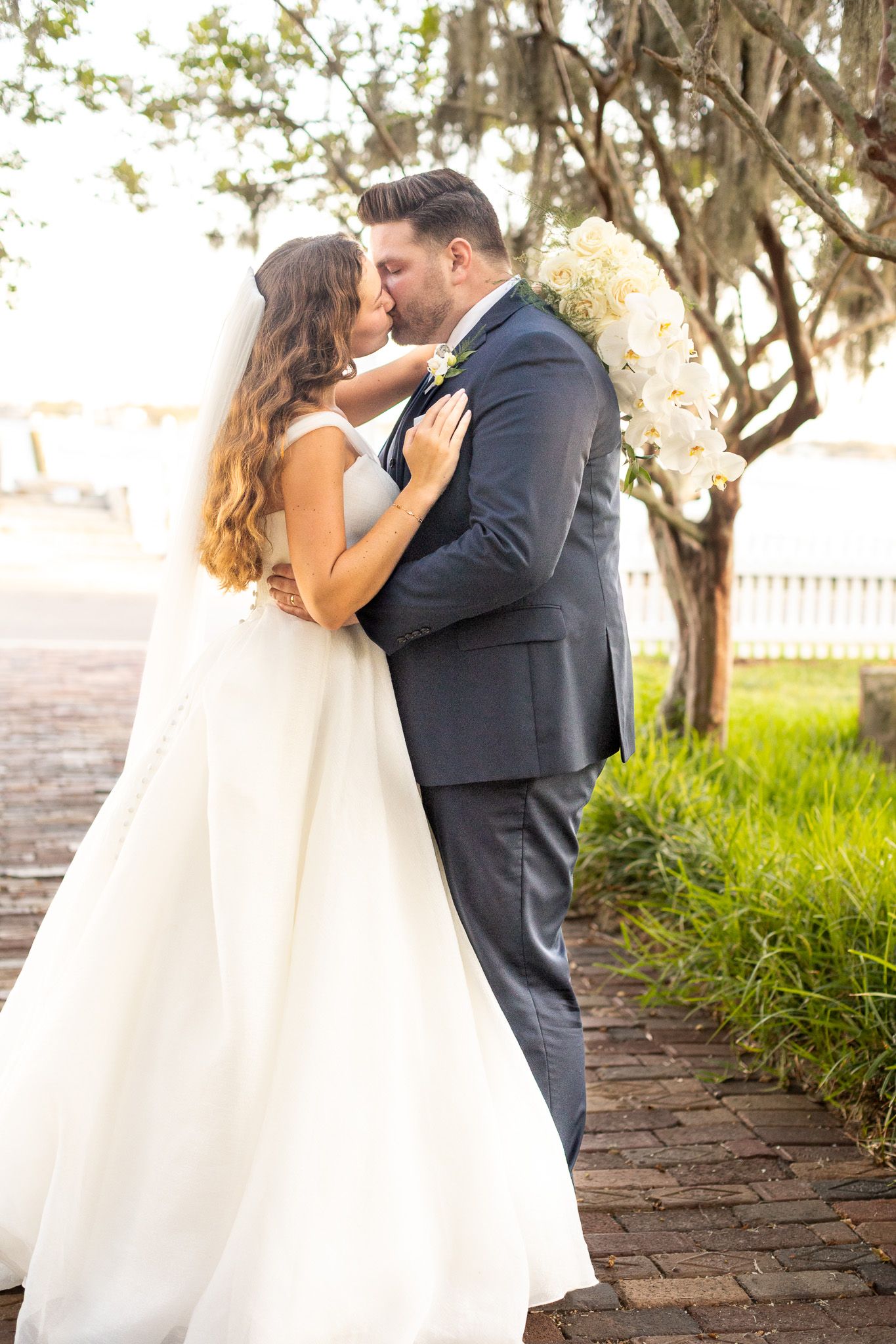 A romantic wedding moment captured on a brick pathway with trees in the background.