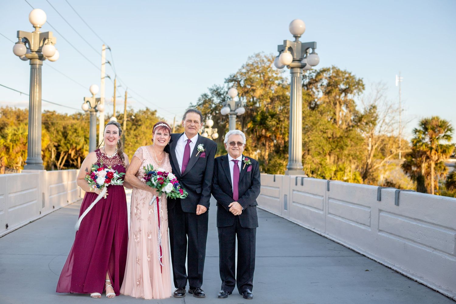 Wedding group photos on bridge with lamp posts during golden hour.