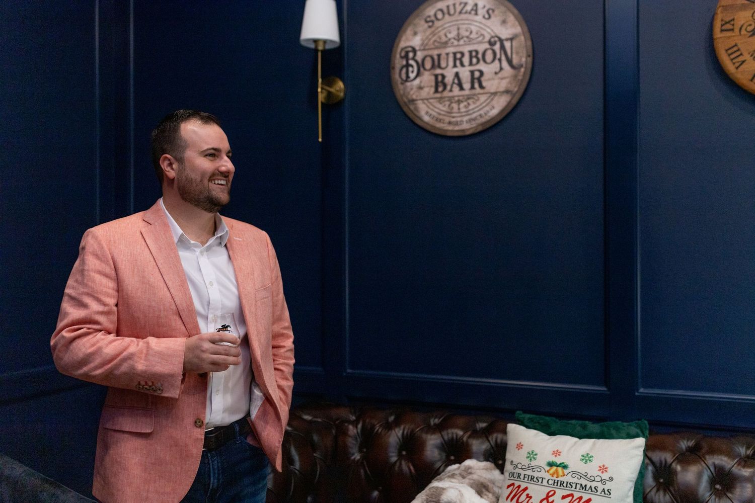 Person in pink blazer stands in front of navy blue wall with bourbon bar decor.