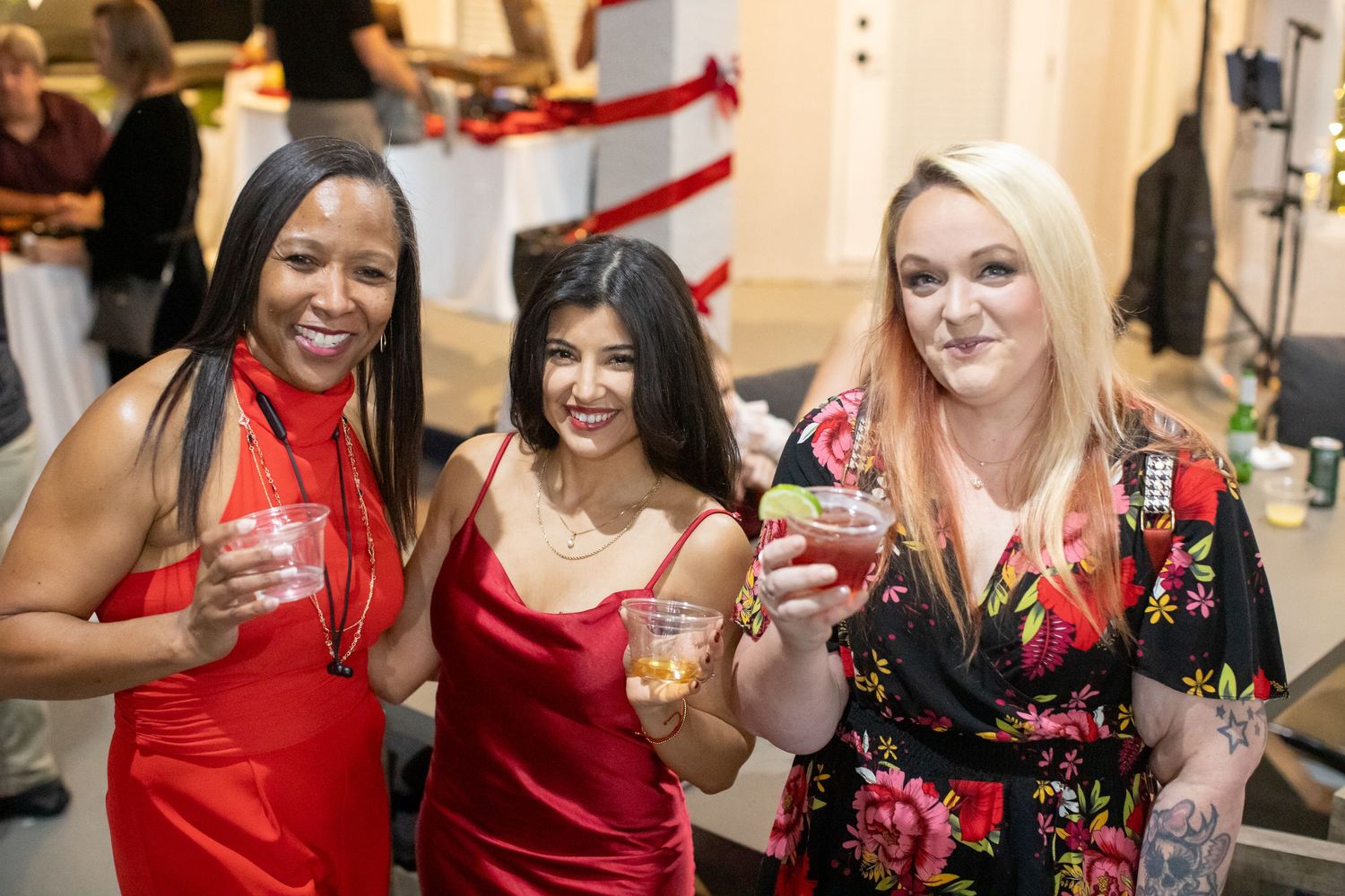 A festive holiday party gathering with people in red dresses enjoying drinks and conversation.