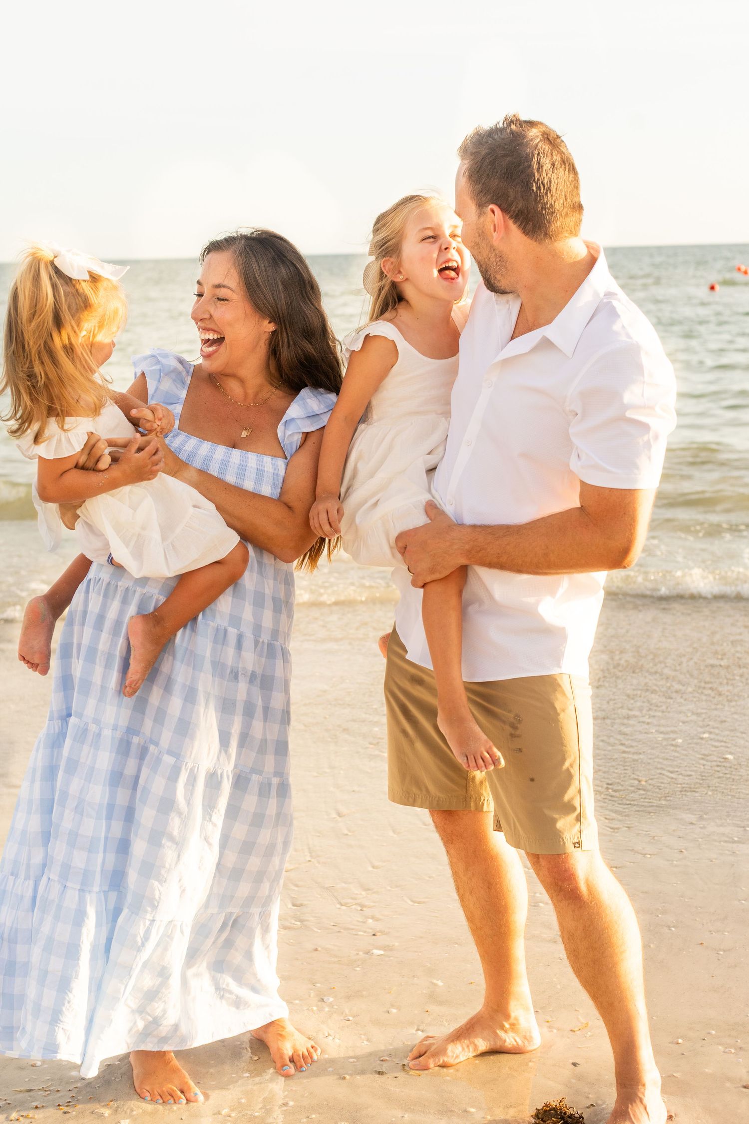Family shares candid laughing moments during their beach photo session at sunset.