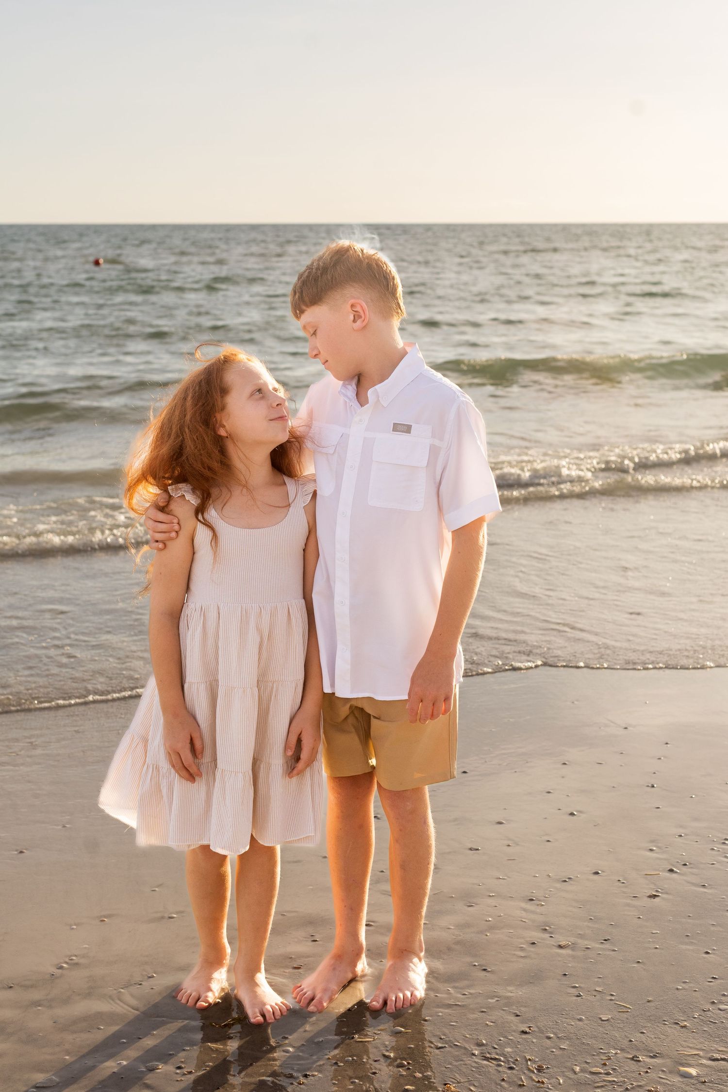 Two children in light summer outfits playing on beach at sunset.