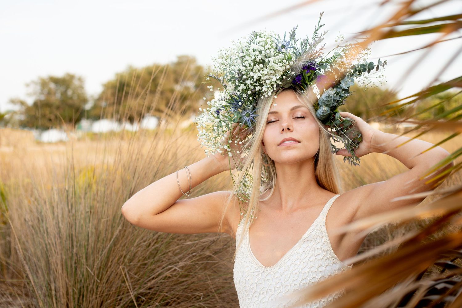 Ethereal portrait in a field with a delicate floral crown and white dress against golden grasses at sunset.