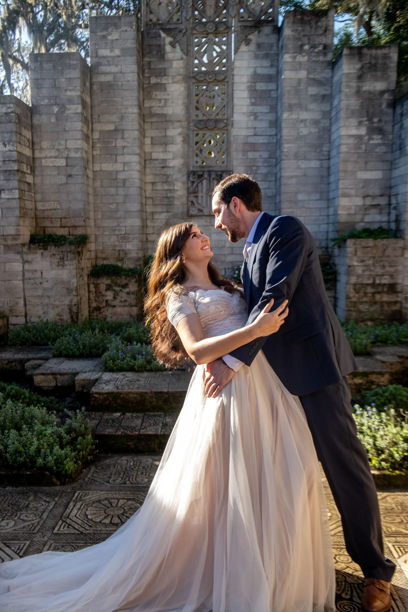 A romantic wedding couple dancing and dipping in front of a stone wall with greenery.