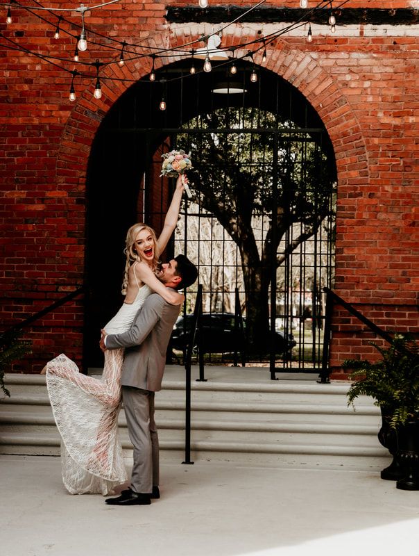 Newlyweds dancing under string lights against exposed brick wall.