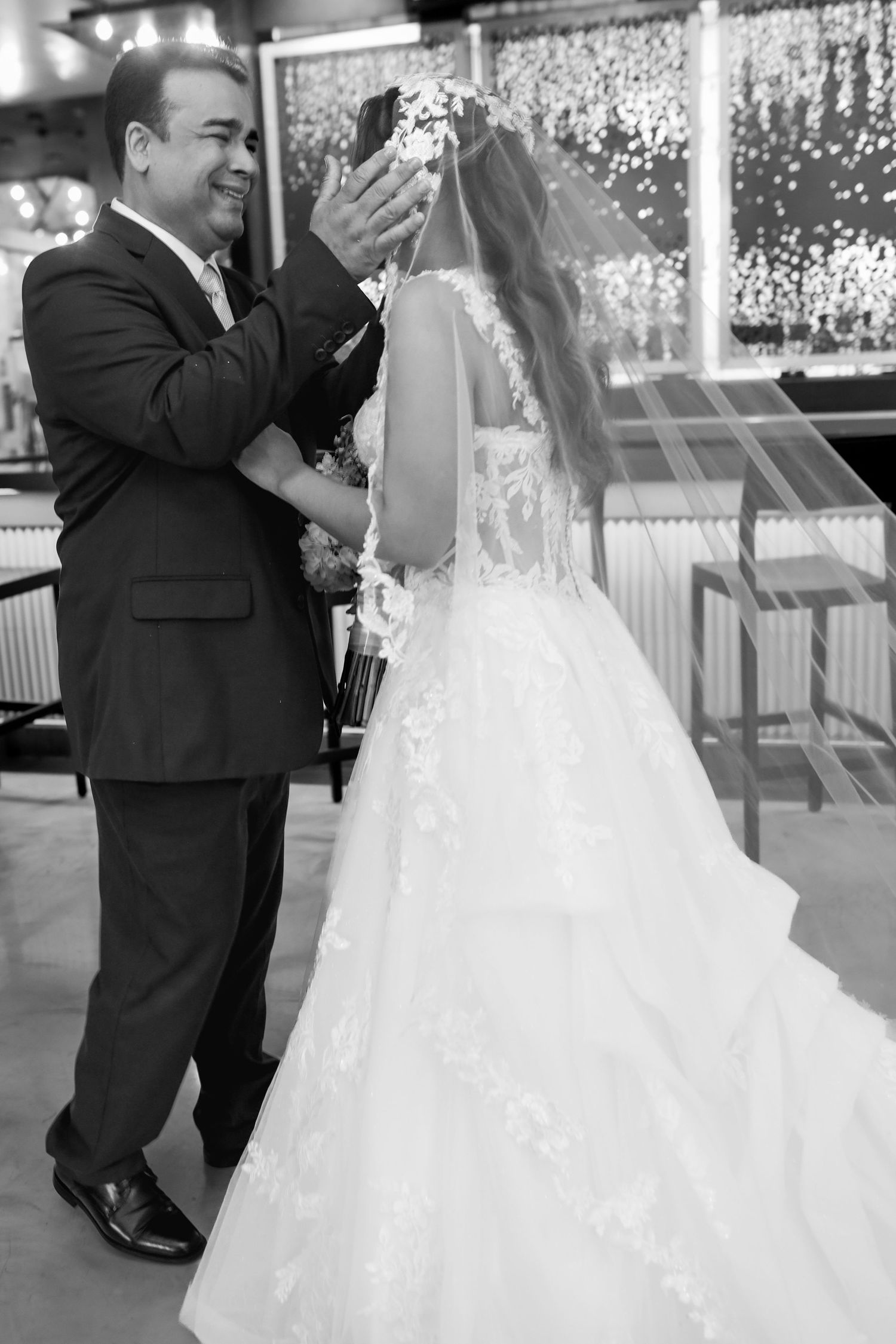 Black and white photo of a groom placing a veil on his bride in a wedding gown during their ceremony.
