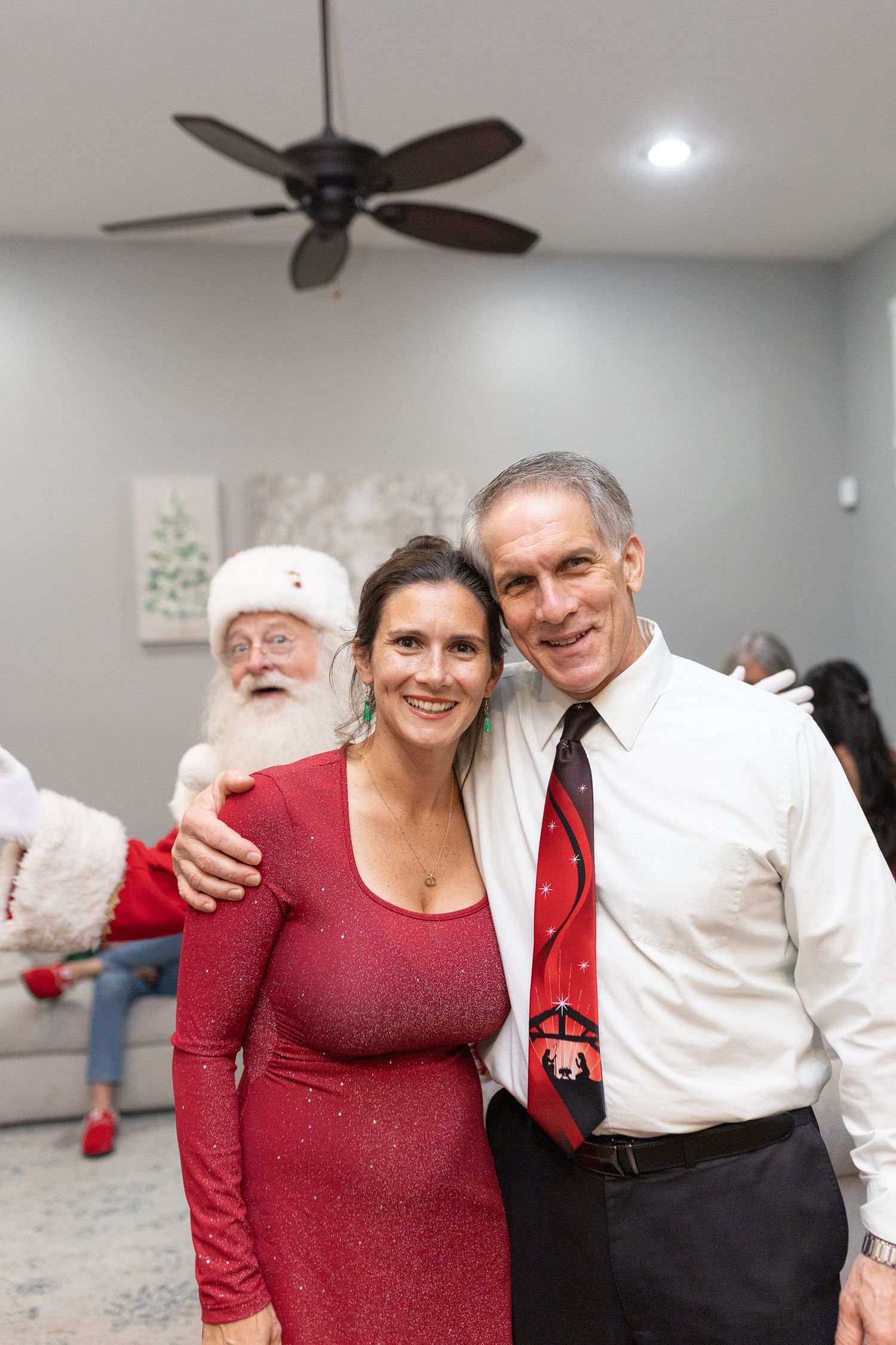 Holiday celebration with people in festive red and white attire under ceiling fans.