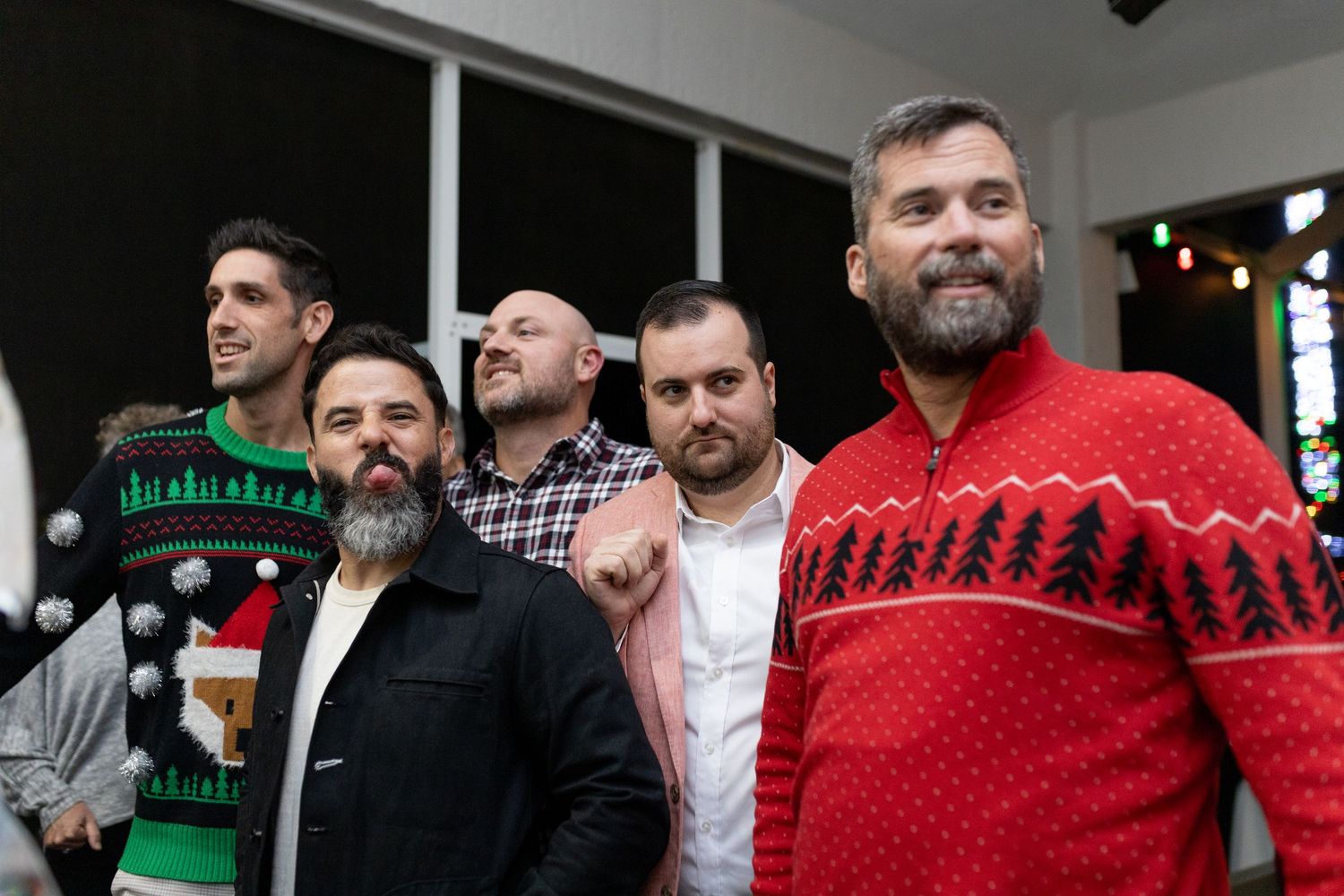 Group wearing festive Christmas sweaters posing together at a holiday party.