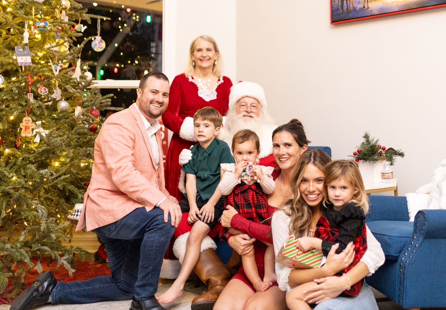 Holiday photo session with family and Santa Claus by decorated Christmas tree and blue couch.