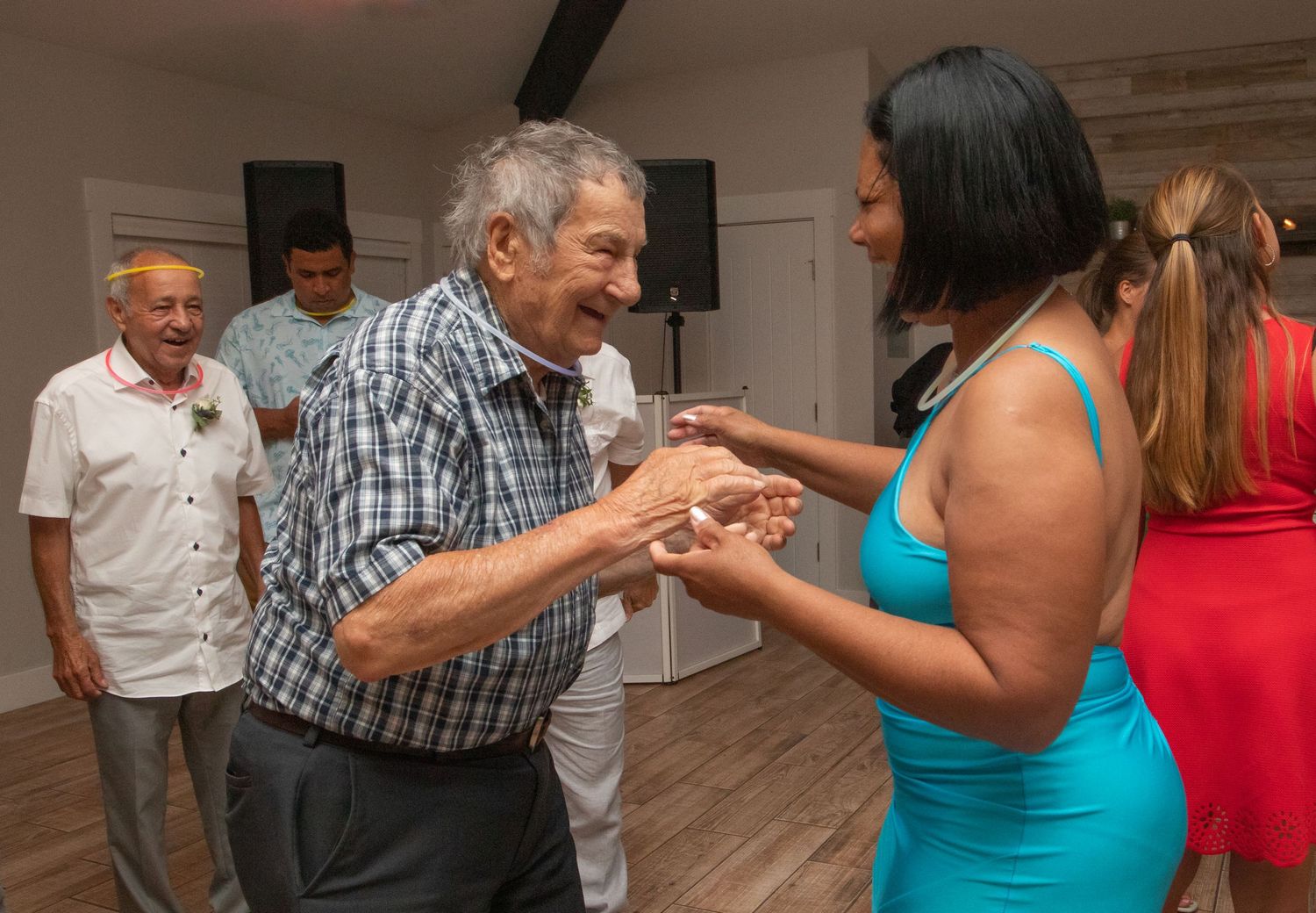 Elderly man dancing with a woman in a blue dress at an indoor celebration event.