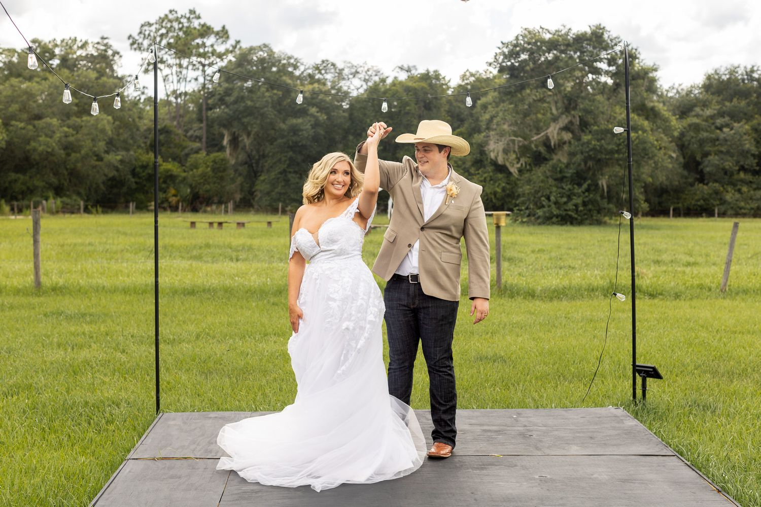 Wedding couple poses on rustic wooden bridge surrounded by green countryside.