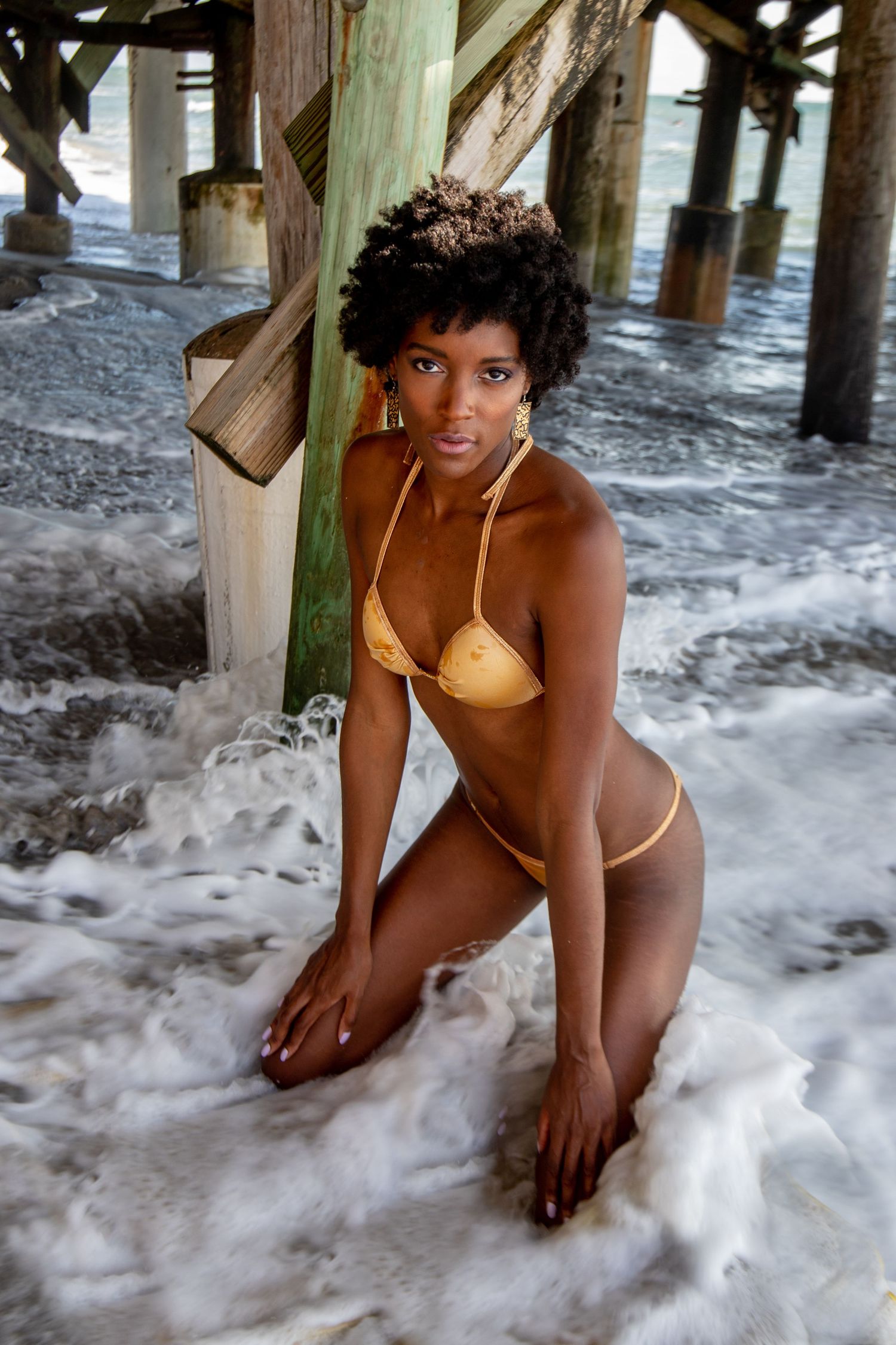 Swimwear photography with natural lighting under beach pier and ocean foam.