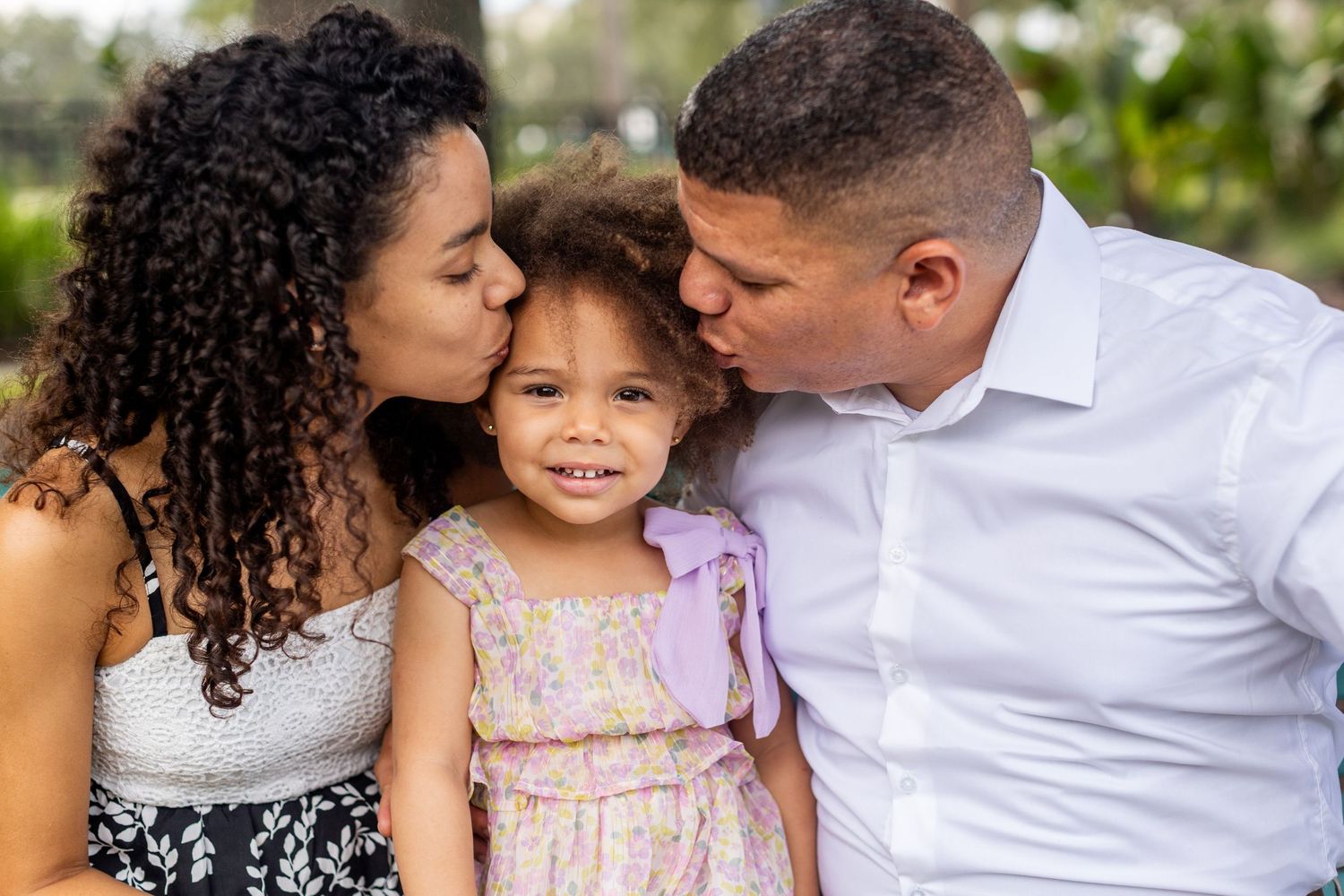 Family shares tender moment together outdoors in coordinated white and pink outfits.