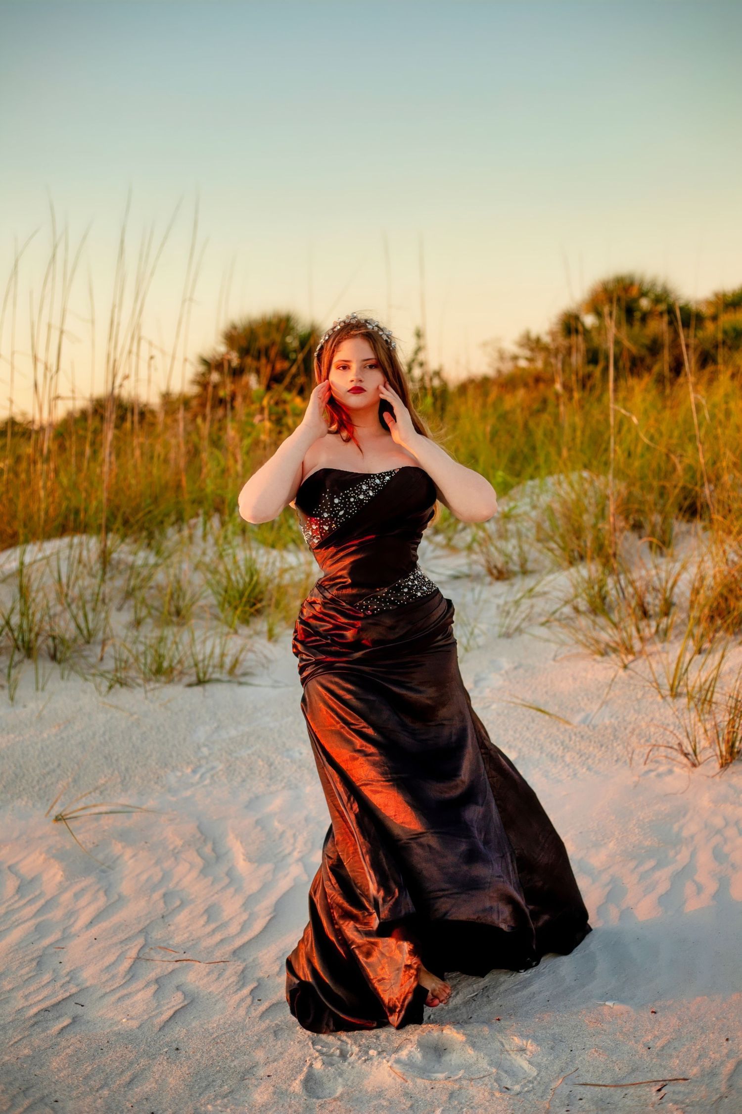 Dramatic beach photoshoot with a flowing burgundy dress against white sand dunes at sunset.