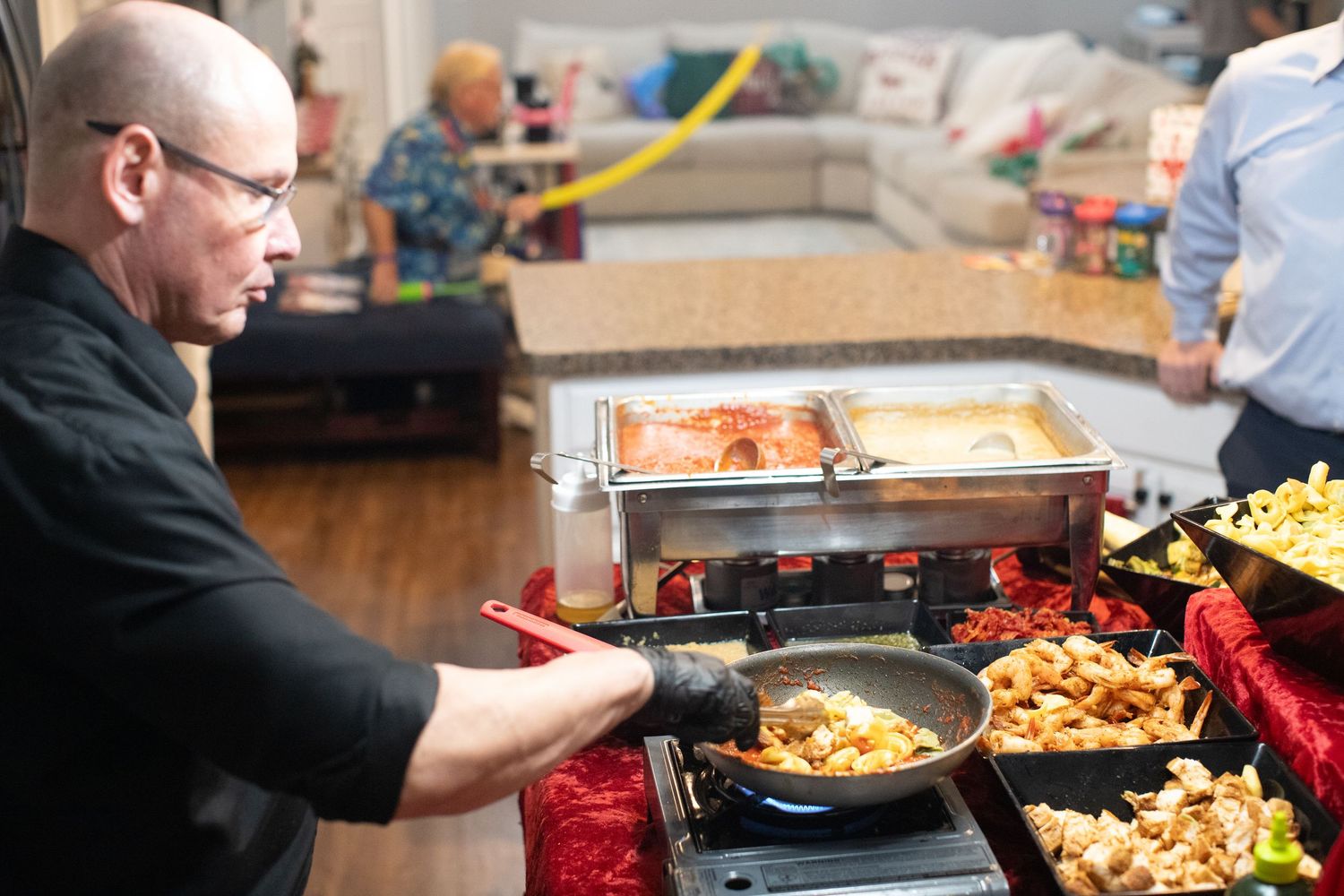 Several people prepare food in a kitchen with various dishes and ingredients spread across the counter.