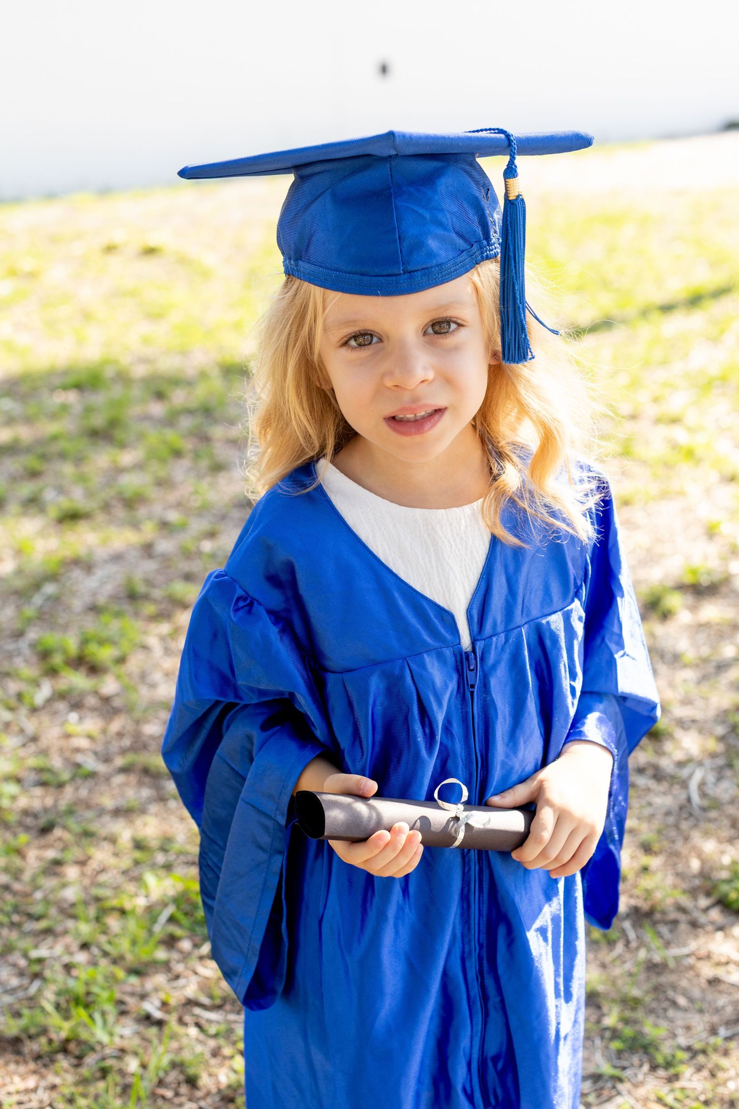 Graduate in royal blue cap and gown holding diploma during outdoor photo session.