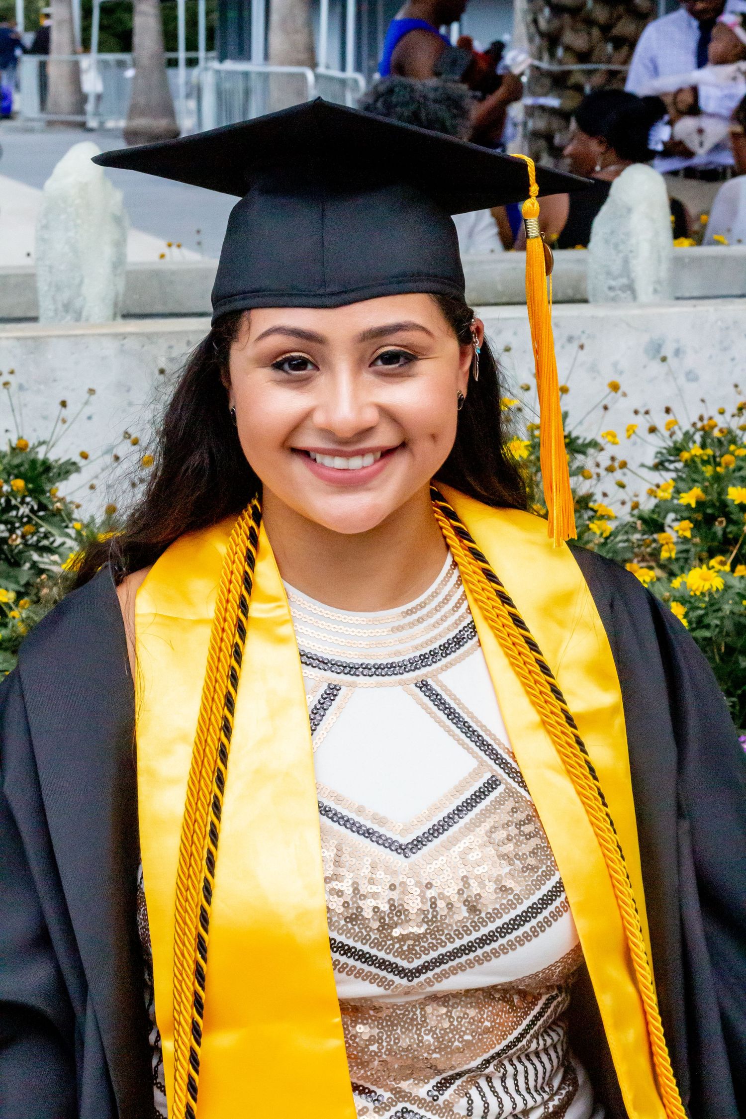 Graduate wearing black cap and gold stole poses for graduation photos outdoors.