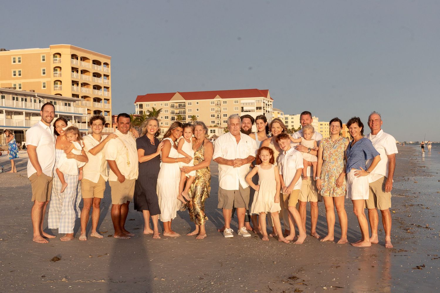 Large group in white and neutral clothing poses together on beach at sunset.
