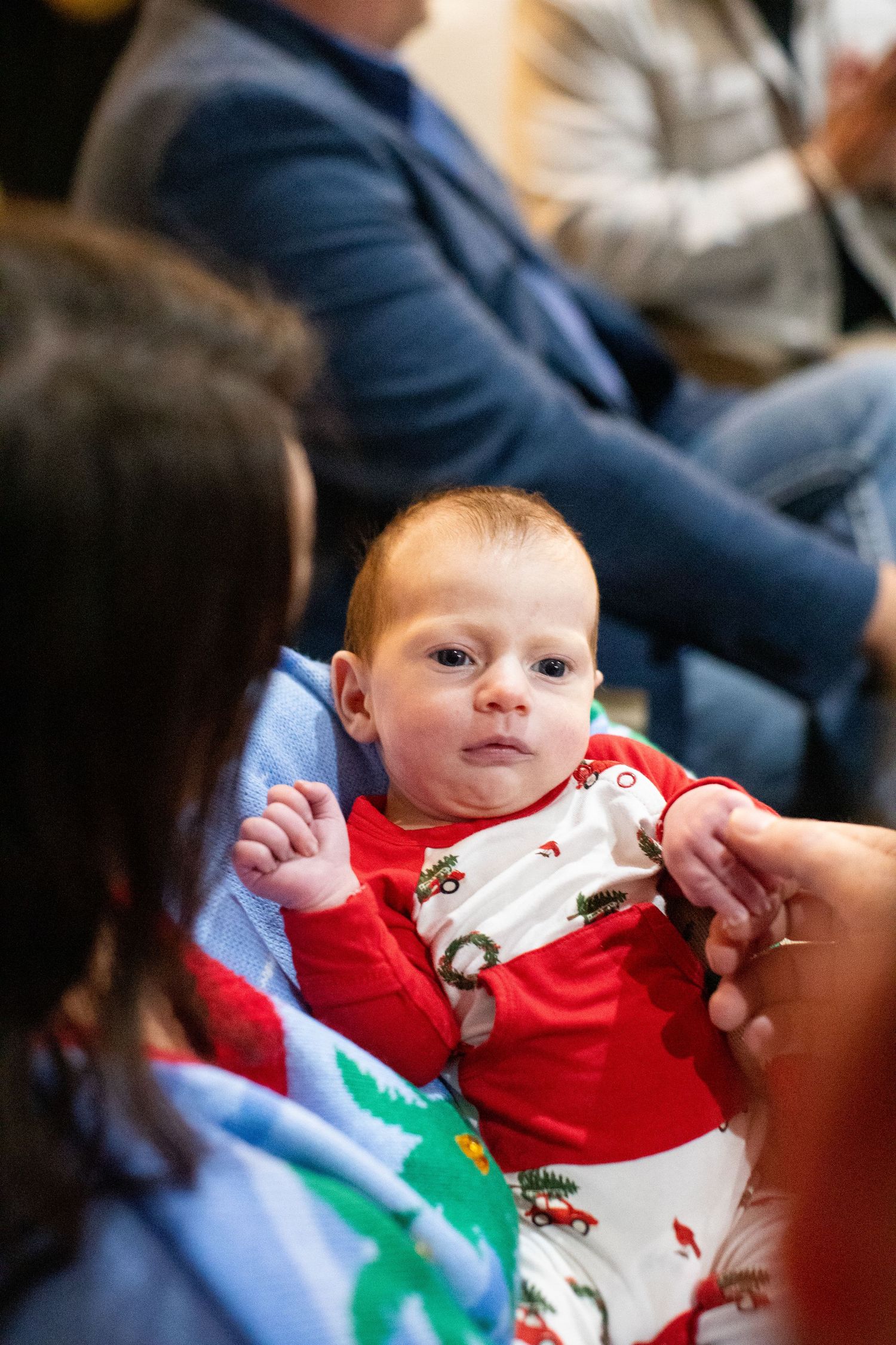 Small infant in holiday attire being held during a Christmas celebration.