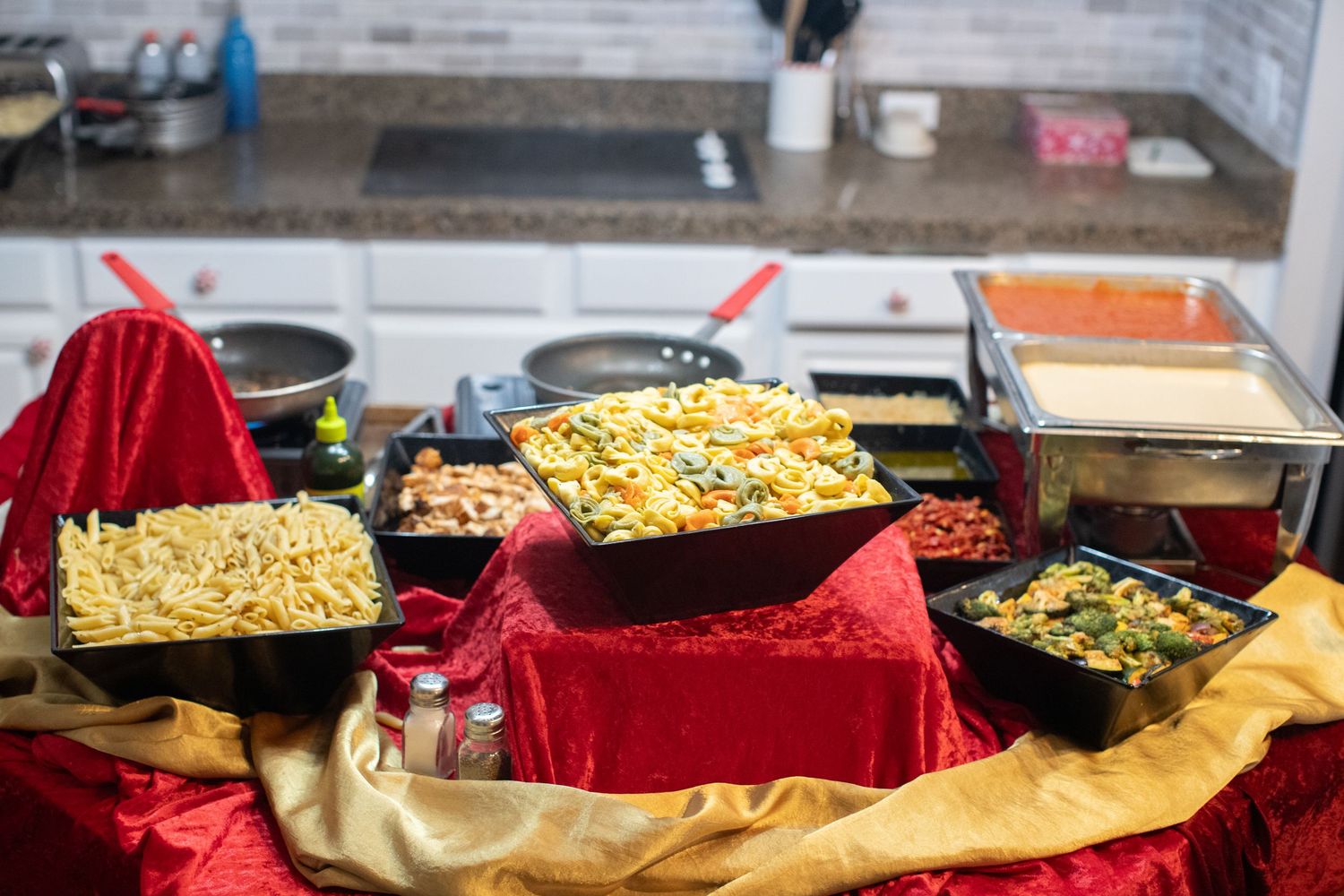 Buffet table with various hot dishes in serving pans with red decorative linens.