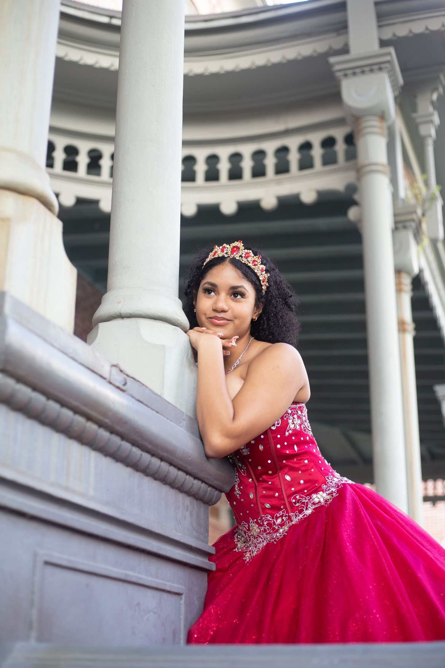 Stunning red quinceañera dress photographed against white colonial pillars.