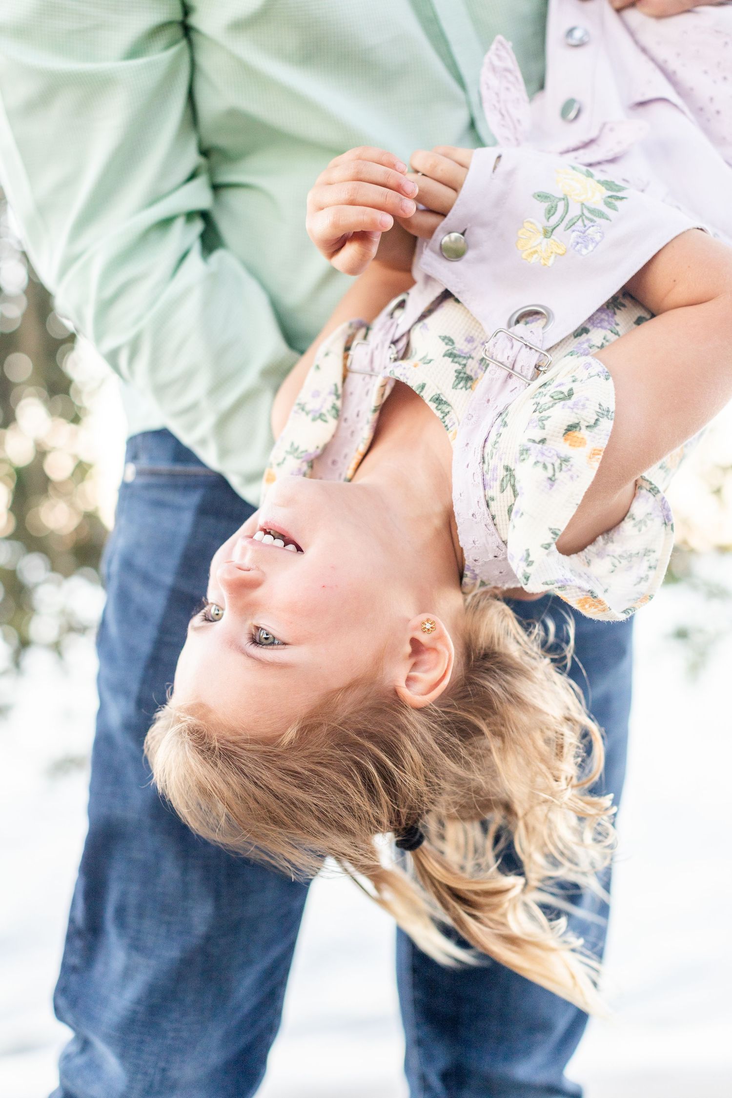 A joyful child being held upside down by an adult outdoors in a snowy winter setting, laughing and smiling.