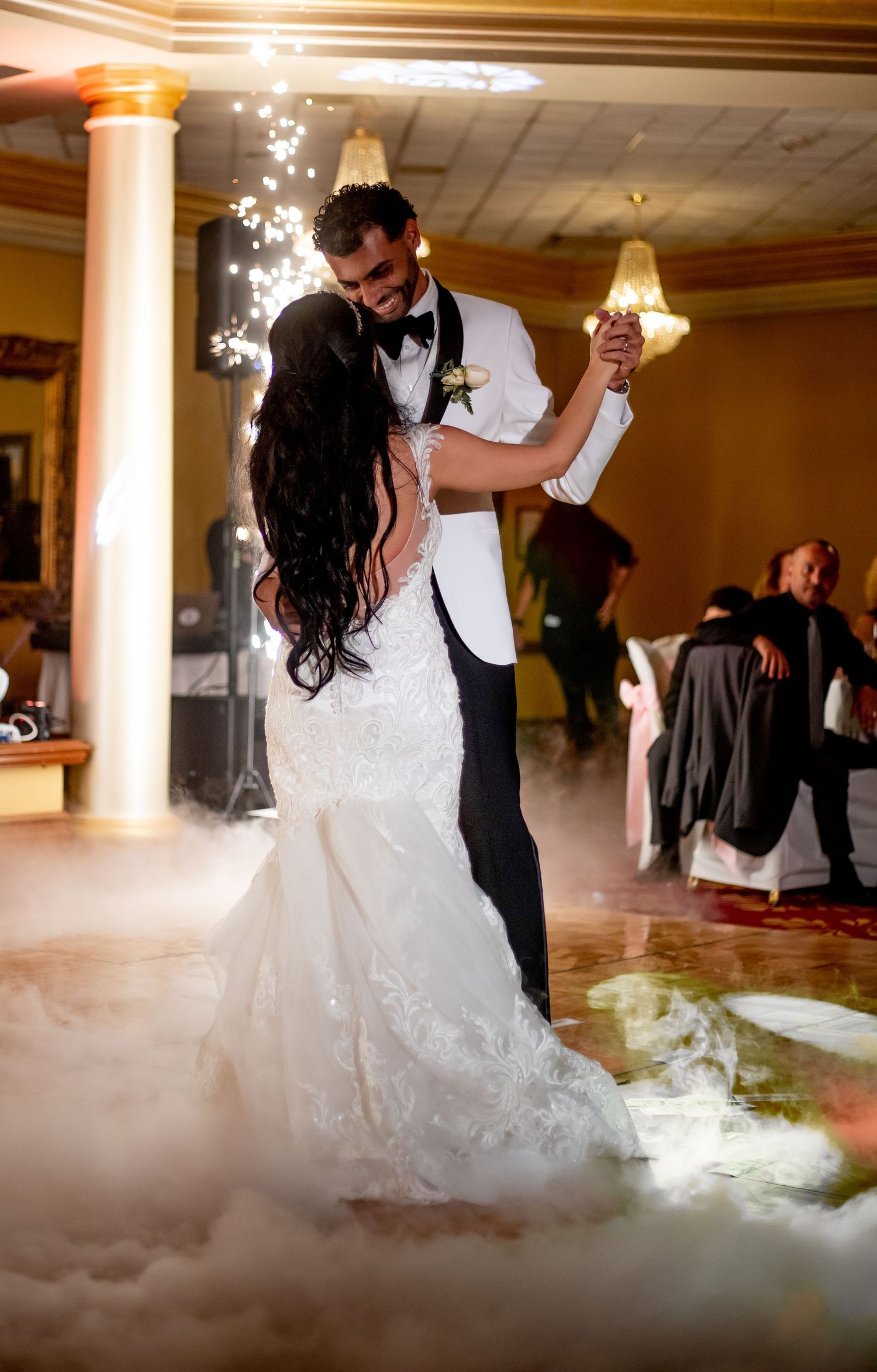 Bride and groom share first dance surrounded by romantic fog and sparkling lights in elegant wedding reception venue.