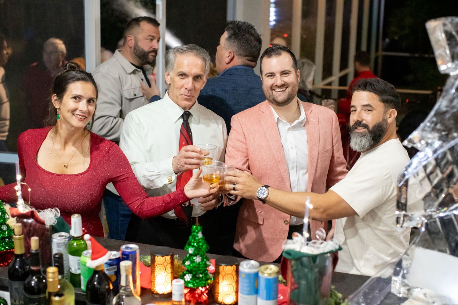 Group toasting with drinks at holiday party with bar setup in background.