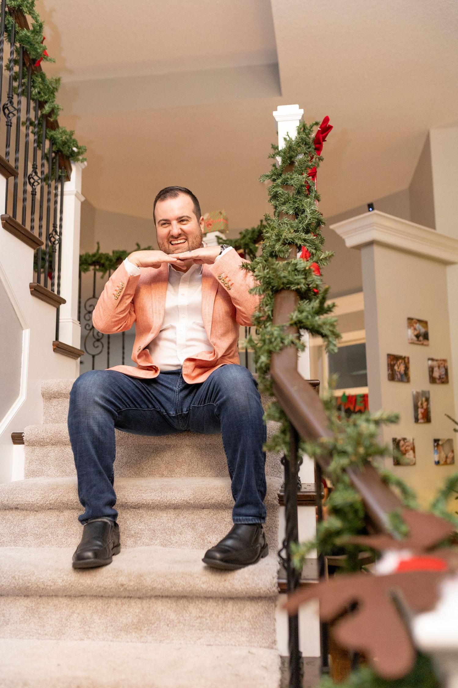Someone wearing a peach-colored blazer and jeans sits on carpeted stairs decorated with holiday greenery.