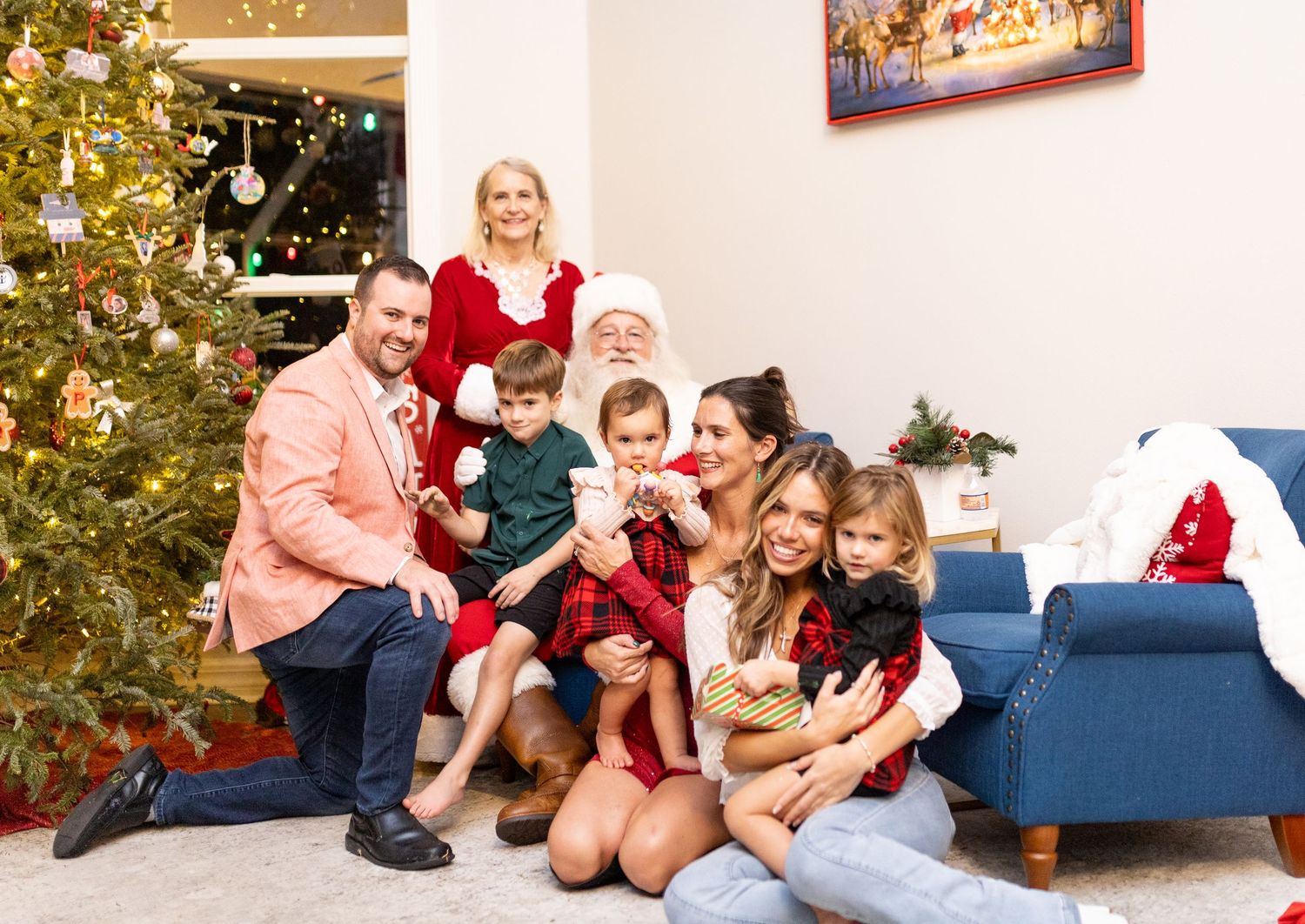 Holiday photo session with family and Santa Claus by decorated Christmas tree and blue couch.