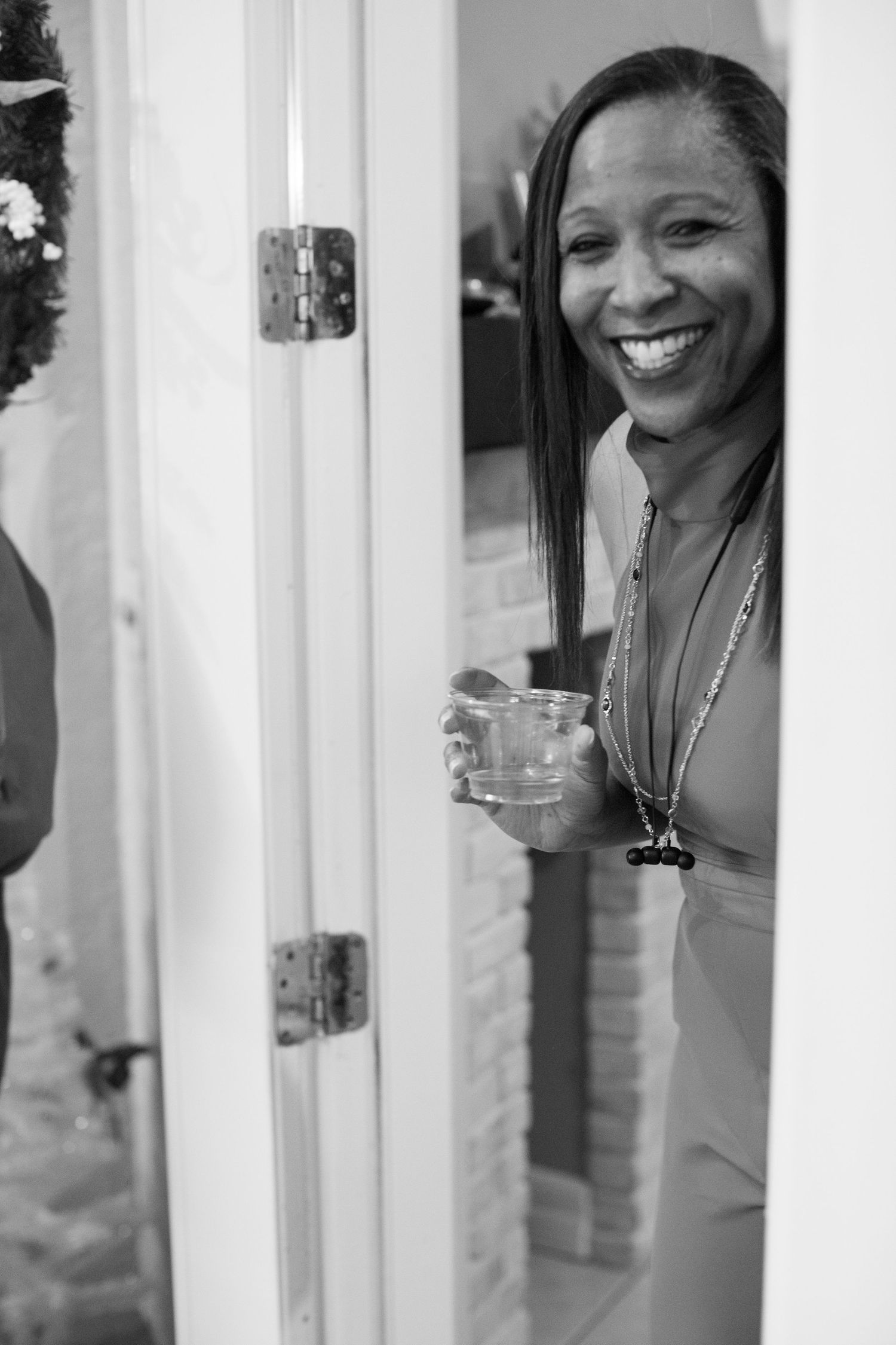 Person in red dress smiling through doorway with drink in hand.