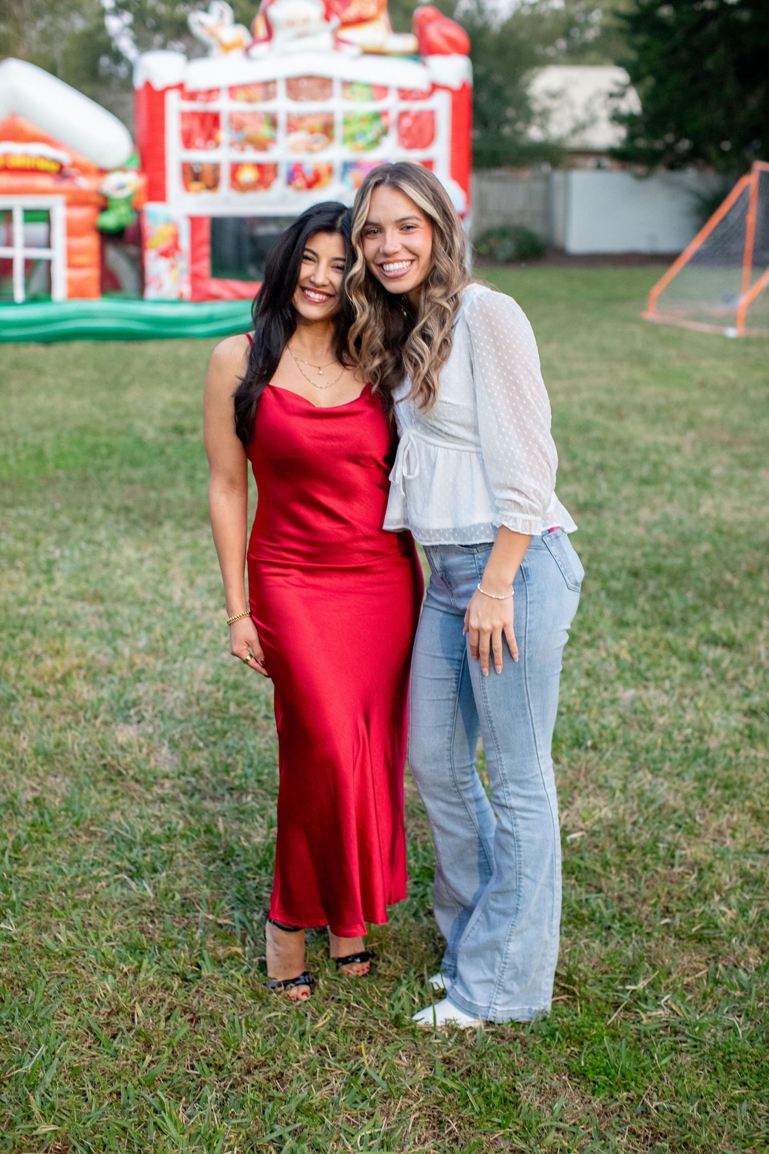 Friends pose together on grass with carnival attractions visible in background during outdoor event.