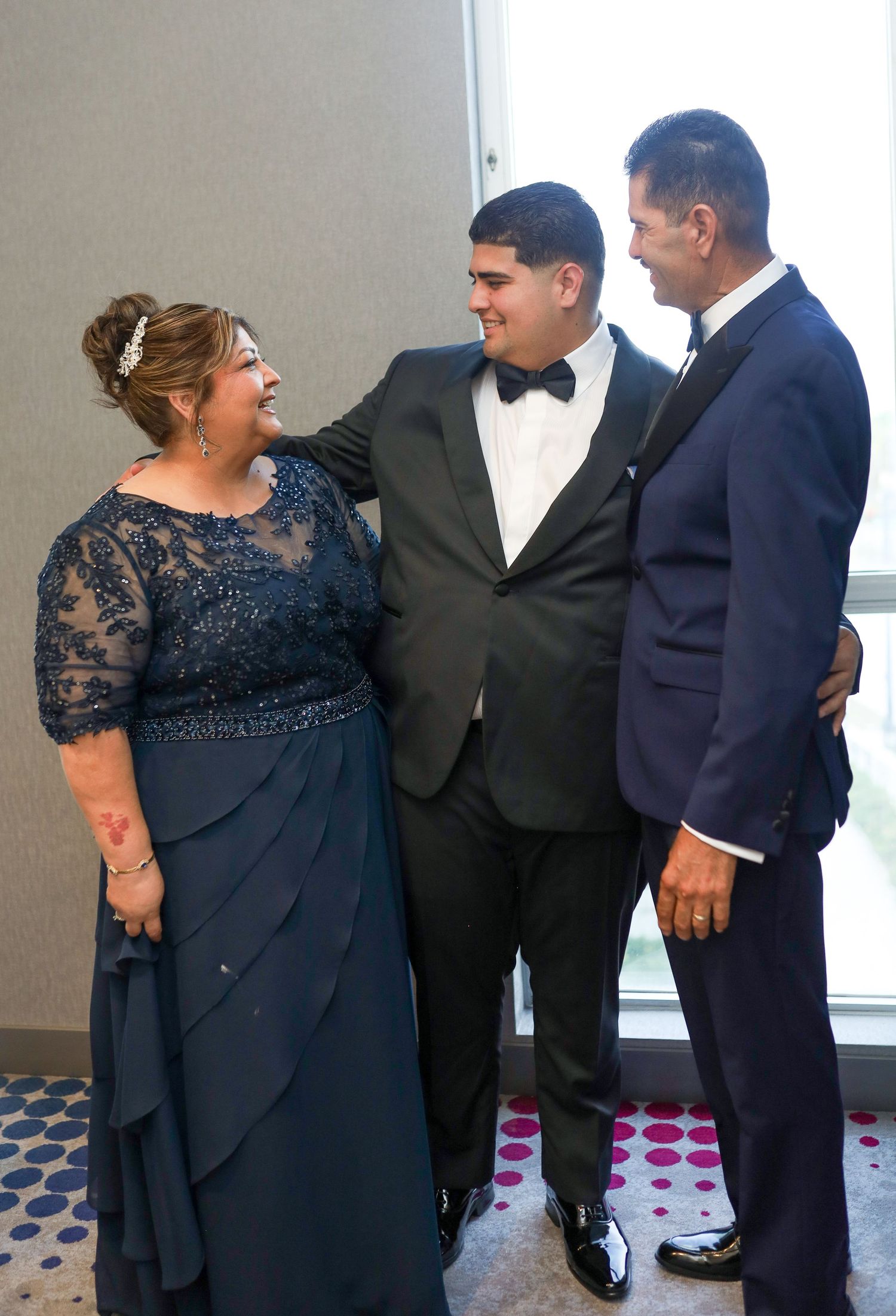 Family of three dressed formally in navy and black attire smiling together at an elegant event.