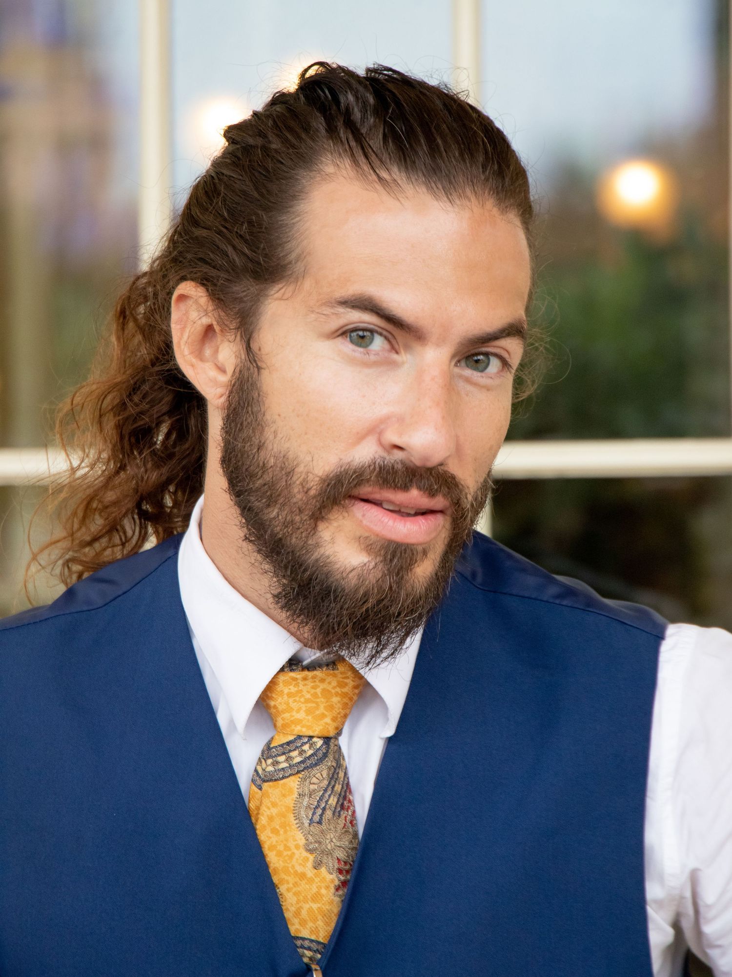Person in business attire with navy vest and yellow tie poses by window.