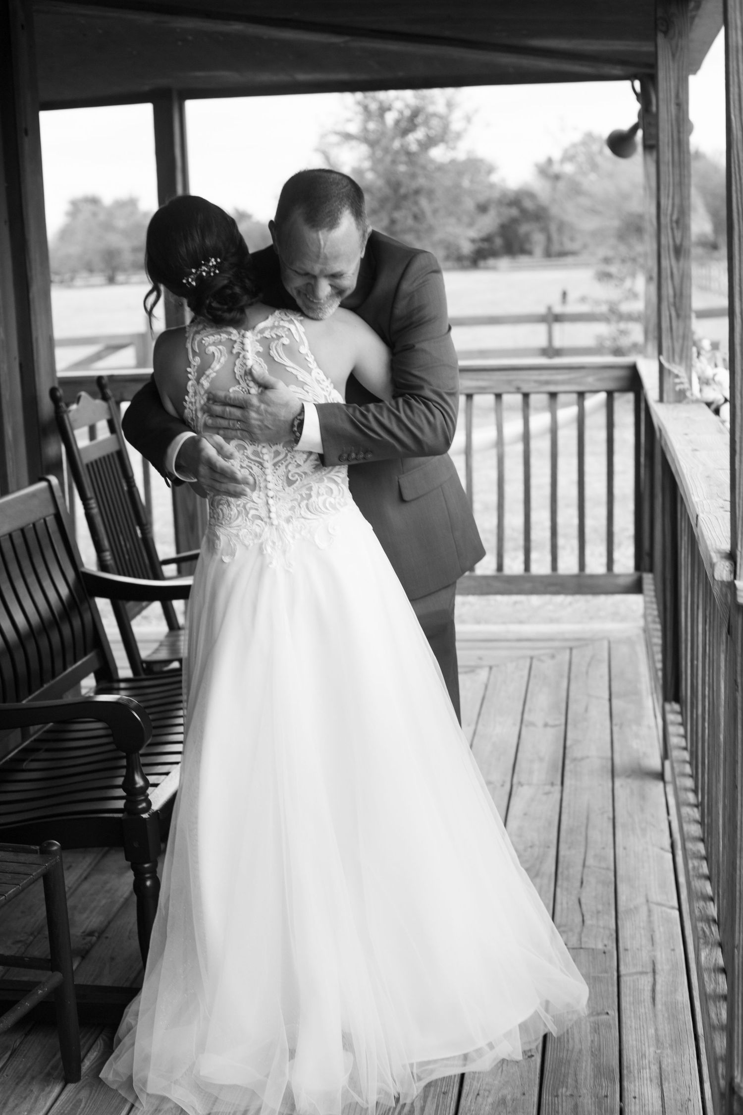 Black and white photo of bride and groom sharing a tender embrace on a wooden porch during their wedding day.
