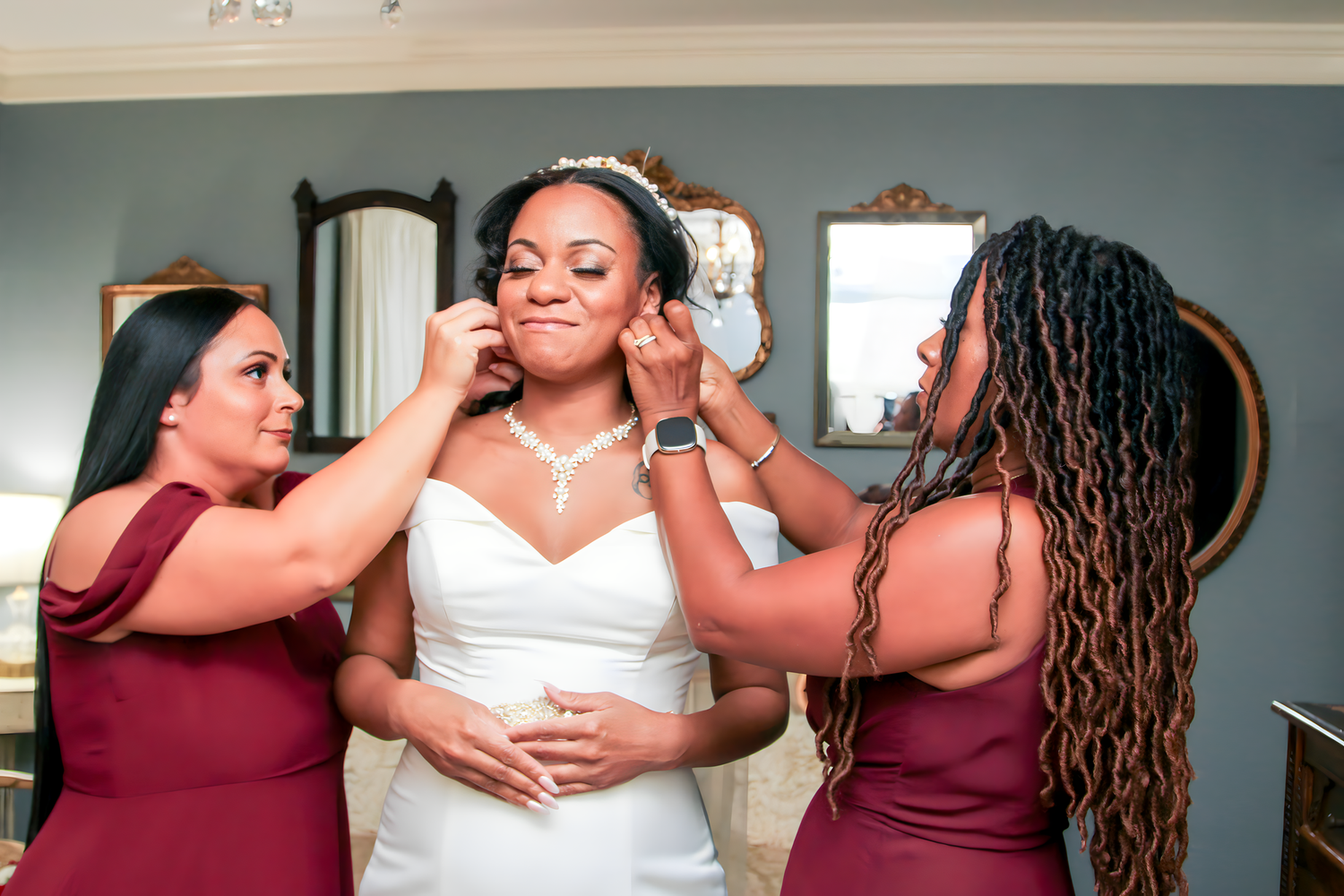 Bridesmaids in burgundy dresses help with wedding preparations.