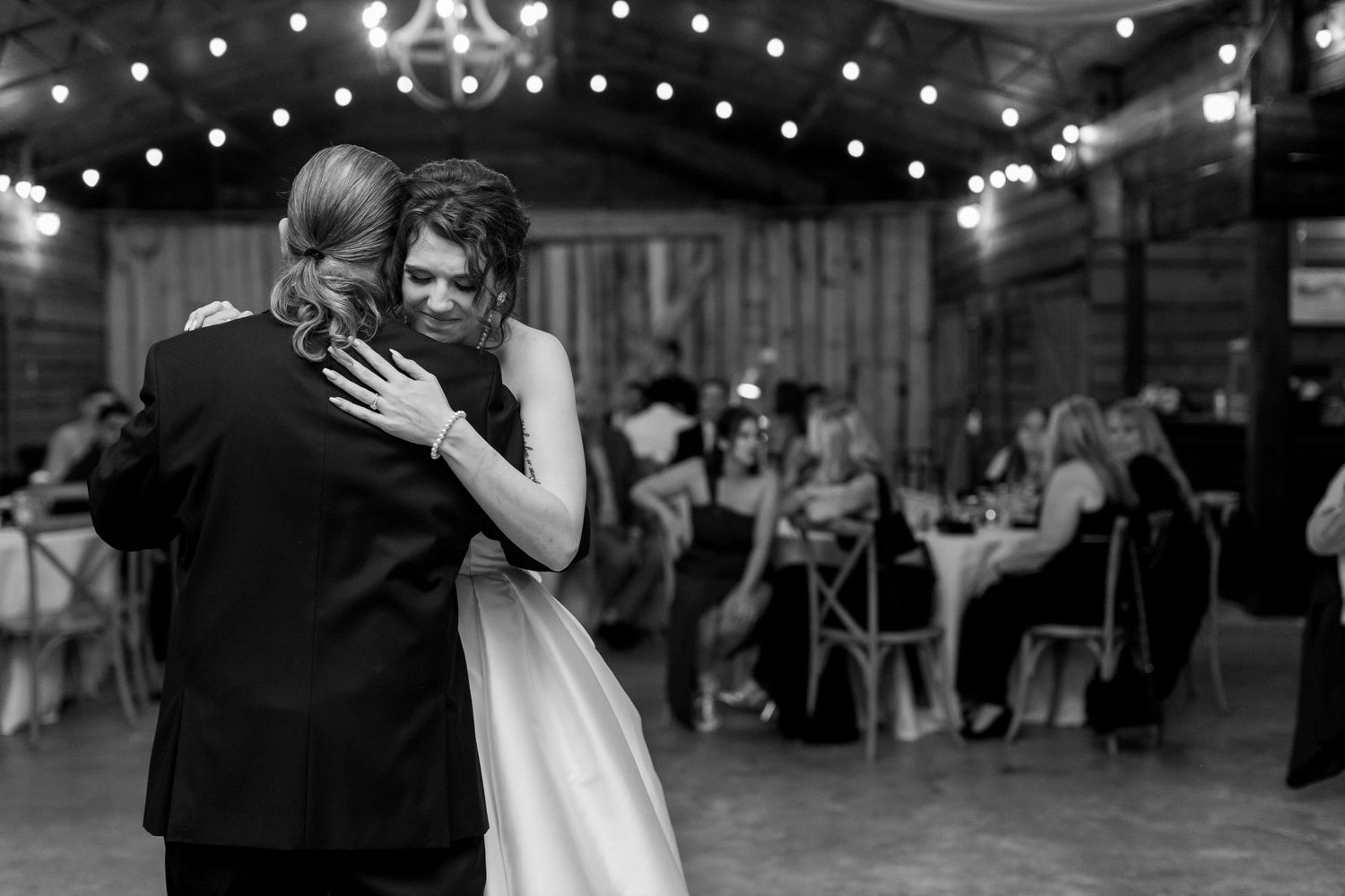 Wedding reception dance in a rustic barn venue with string lights overhead.